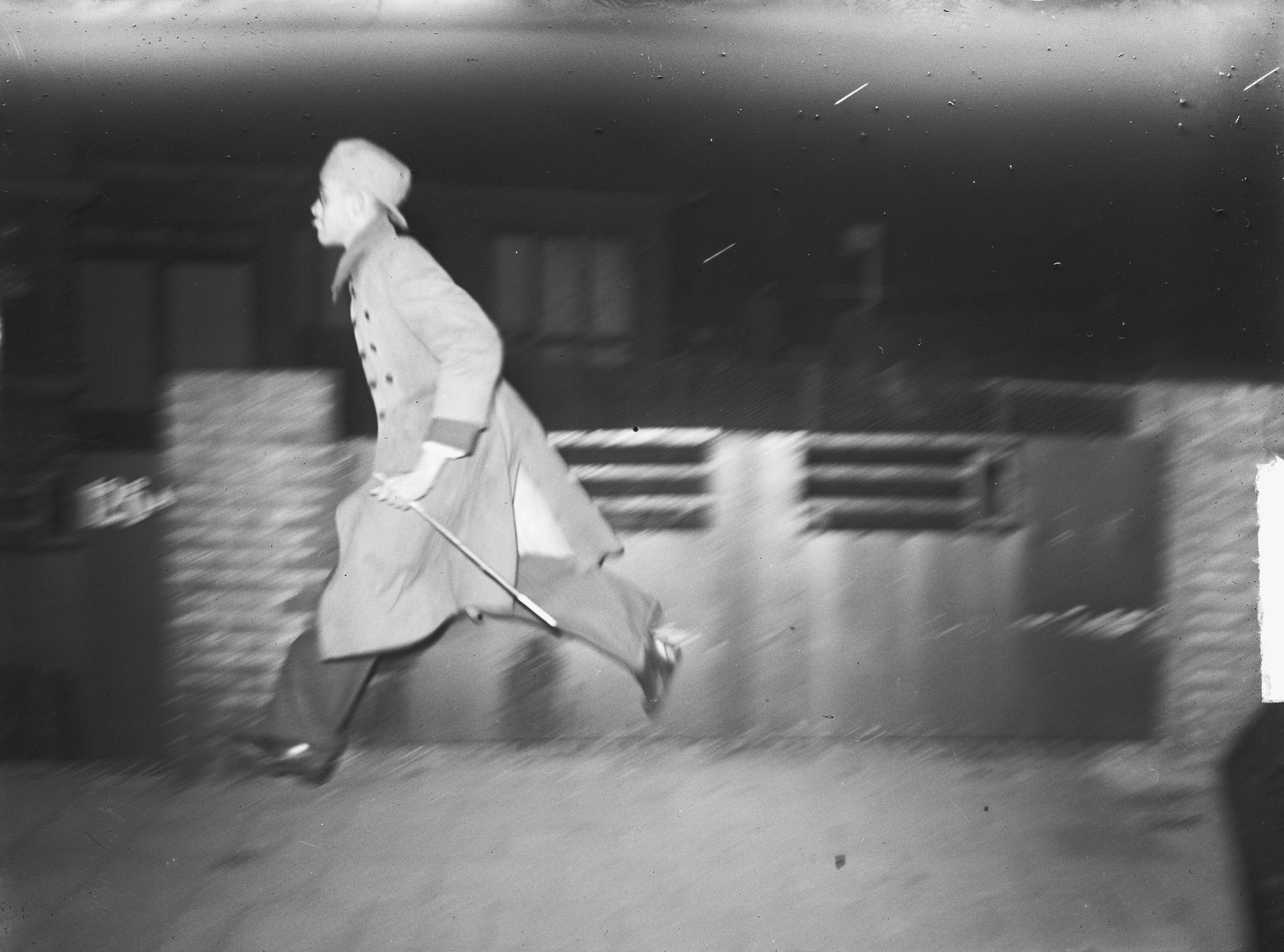 Fotocollectie Anefo — Studentenongeregeldheden In Den Haag [een jonge man met omgedraaide pet en lange jas met in zijn linkerhand een stok, rent over straat] — Foto: Oorschot, […] van / Anefo. Licentie: Set B: Rechtenvrij / Publiek Domein. Bron: Nationaal Archief. http://hdl.handle.net/10648/a8cf2096-d0b4-102d-bcf8-003048976d84