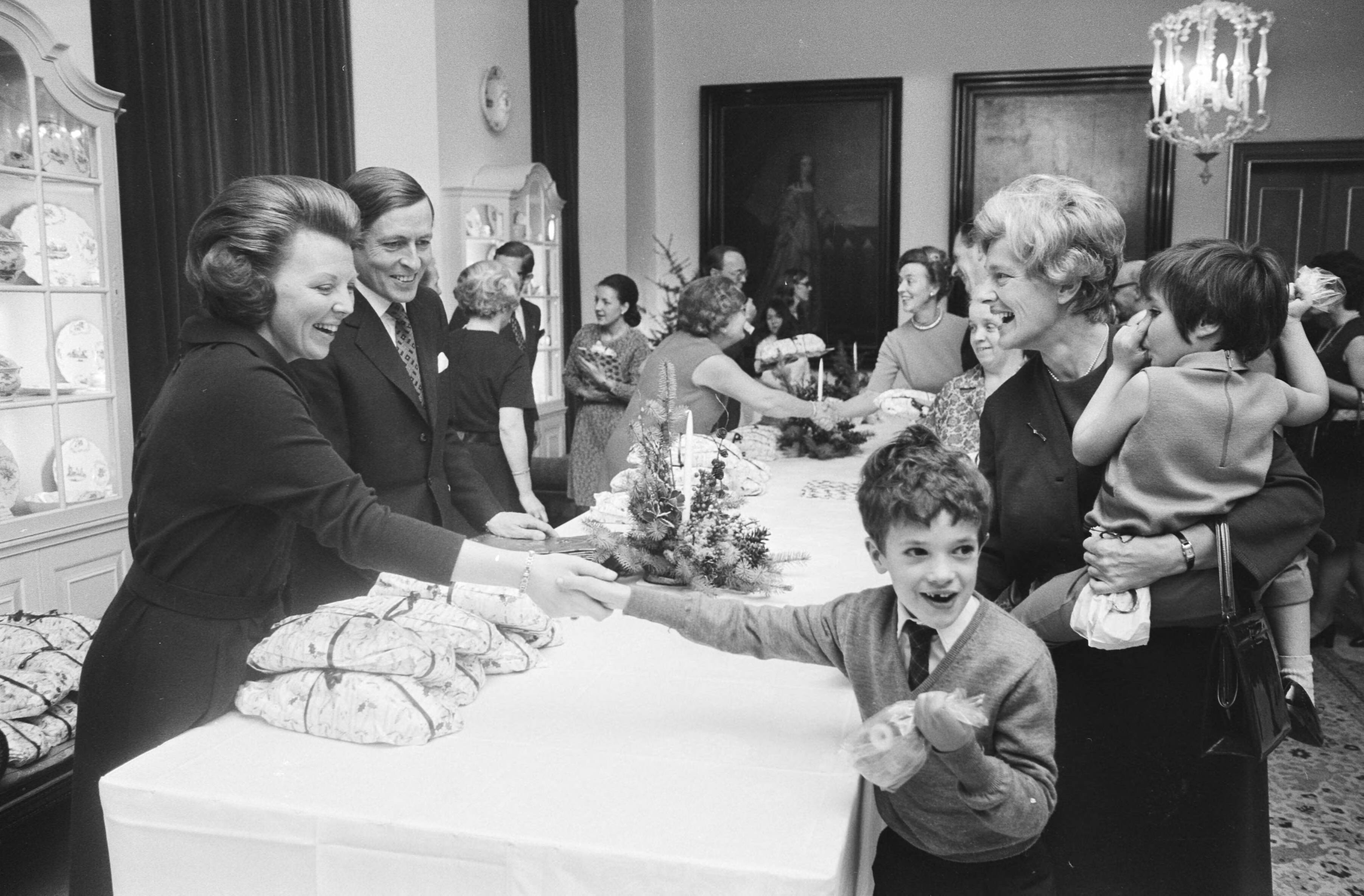 Fotocollectie Anefo — Koninklijk Huis houdt jaarlijks Kerstfeest voor personeel op Huis ten Bosch , Den Haag ; Prinses Beatrix en Prins Claus delen brood uit / — Foto: Mieremet, Rob / Anefo. Licentie: Set B: Rechtenvrij / Publiek Domein. Bron: Nationaal Archief. http://hdl.handle.net/10648/abae288e-d0b4-102d-bcf8-003048976d84