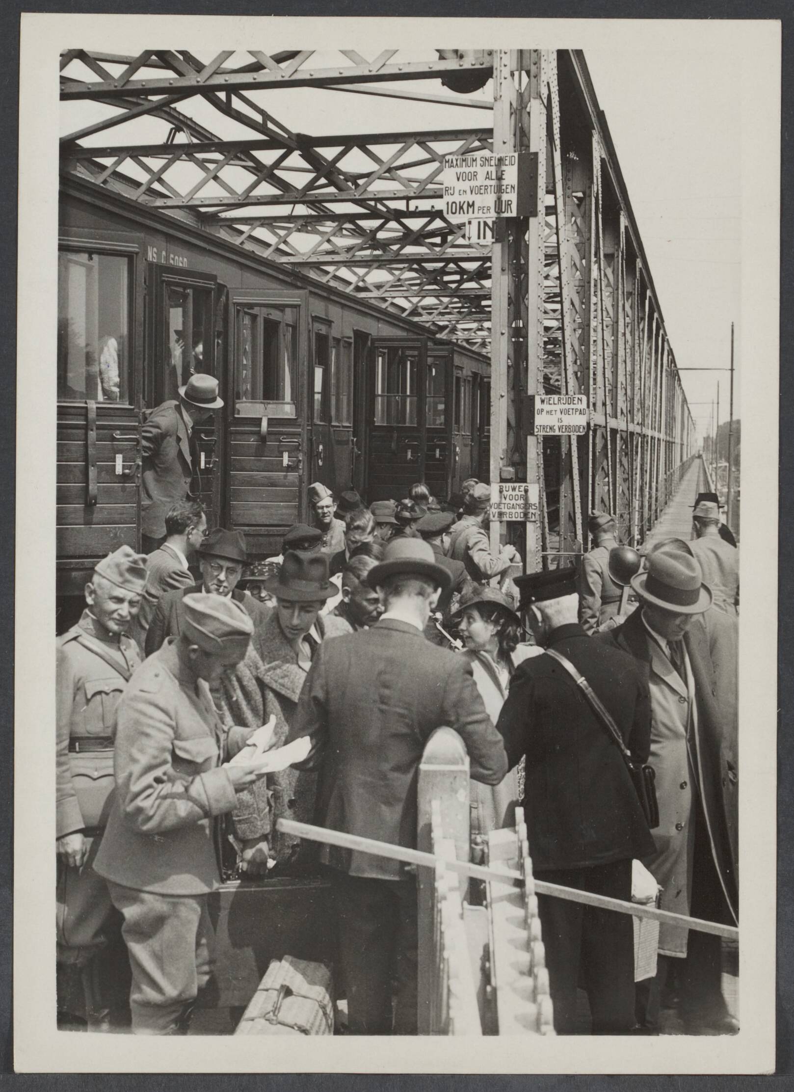 Vervoer — Deventer, 23 mei 1940. De Nederlandse Spoorwegen doet alle mogelijke moeite om de reizigers ter wille te zijn. Zo kunnen b.v. vanaf heden de reizigers uit de richting Apeldoorn voor Deventer worden vervoerd met de trein tot de IJsselbrug voor Deventer, en kunnnen dan door op de pont over te stappen, die hen over de IJssel brengt, de stad Deventer bereiken. het overstappen op de IJsselbrug — Foto: N.V. Polygoon. Licentie: Set B: Rechtenvrij / Publiek Domein. Bron: Nationaal Archief. http://hdl.handle.net/10648/b2f9b1ae-ec58-cf57-b912-951c1677b003