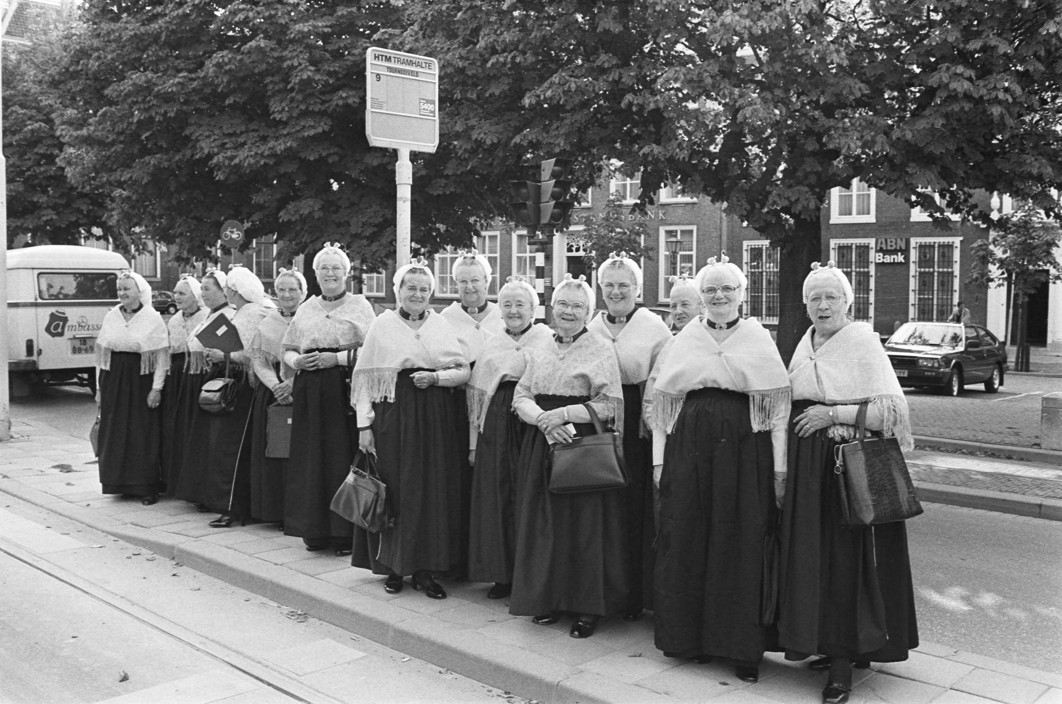 Fotocollectie Anefo — Leden van het Schevenings Visserskoor wachten in Den Haag op de tram — Foto: Antonisse, Marcel / Anefo. Licentie: Set B: Rechtenvrij / Publiek Domein. Bron: Nationaal Archief. http://hdl.handle.net/10648/ad1e5180-d0b4-102d-bcf8-003048976d84