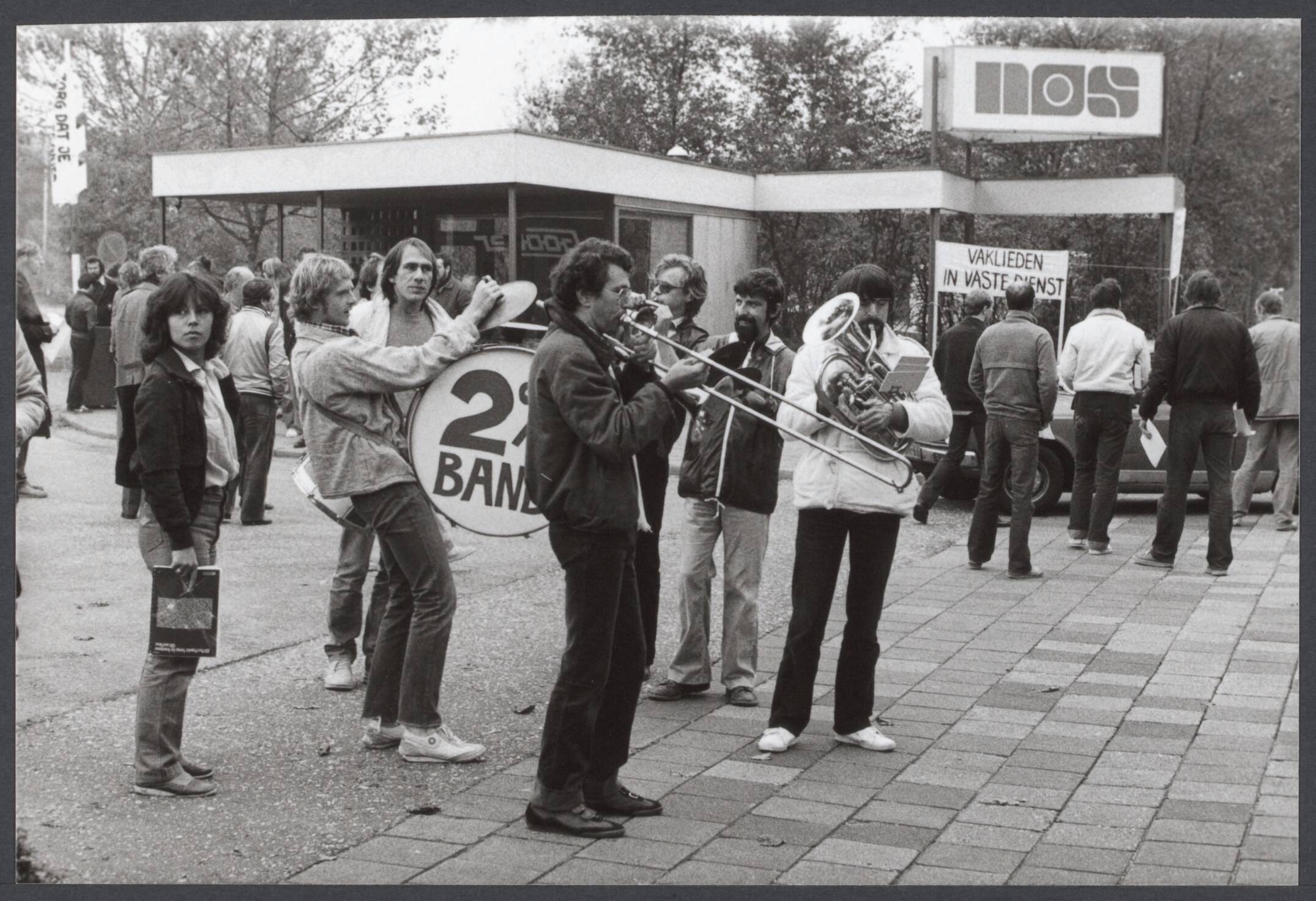 Radioraad, radio- en televisiepolitiek — Vanmorgen werd er door het omroeppersoneel van de NOS in Hilversum gestaakt. Postende omroepmedewerkers voor de toegangspoort van de NOS in Hilversum — Foto: Antonisse, Marcel / Anefo. Licentie: Set B: Rechtenvrij / Publiek Domein. Bron: Nationaal Archief. http://hdl.handle.net/10648/8b68d473-2cb3-d915-3060-7cdc542d1e6c