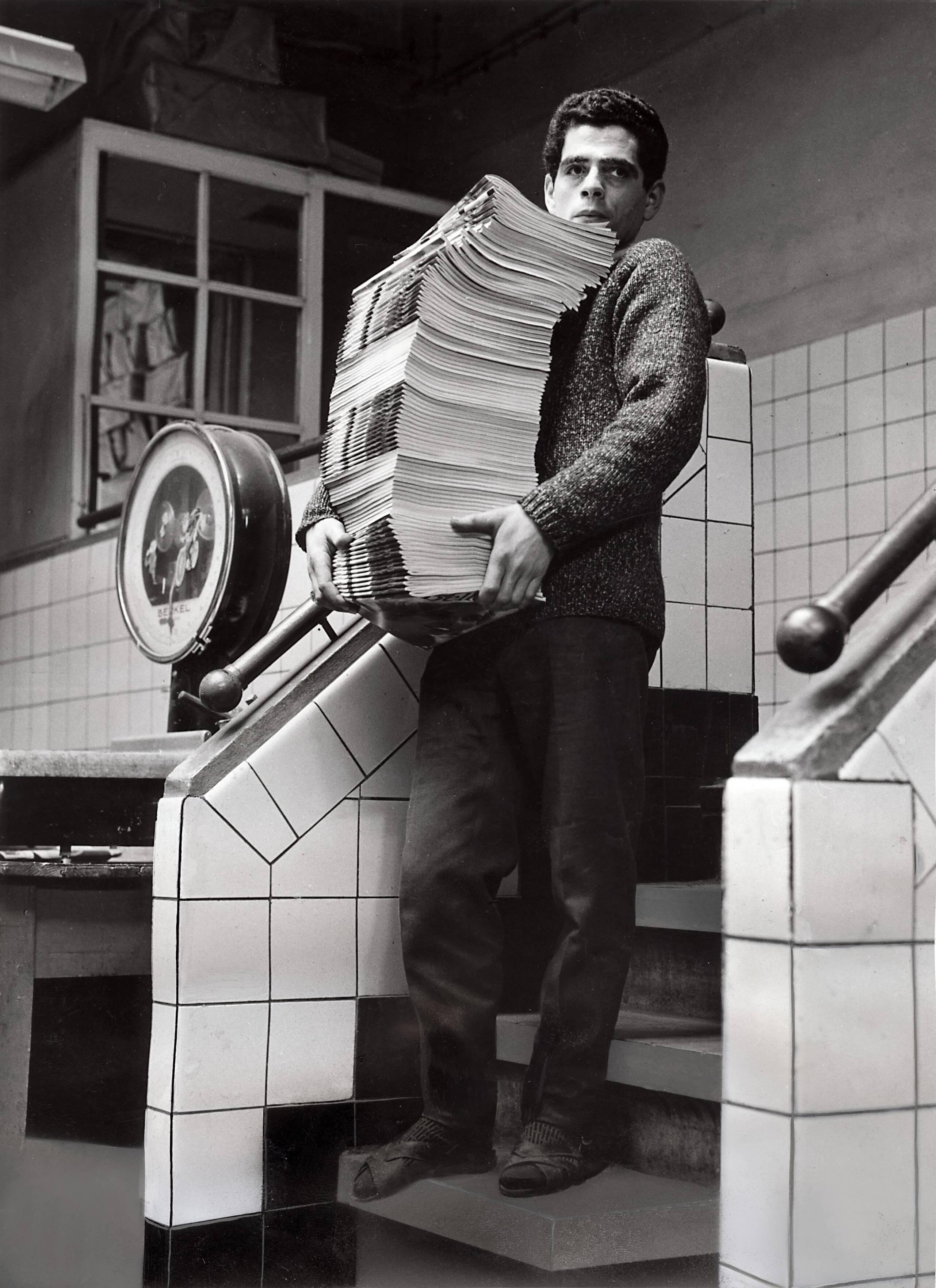 Collectie nader te bepalen — [Serie Bedrijfsvoering Spaarnestad] [een man met een stapel tijdschriften op een trap, links een weegschaal] — Foto: Fotograaf Onbekend / Fotobureau onbekend / Spaarnestad Photo (05887). Licentie: Set B: Rechtenvrij / Publiek Domein. Bron: Nationaal Archief. http://hdl.handle.net/10648/35429da6-4295-a382-e063-6df0900a6686