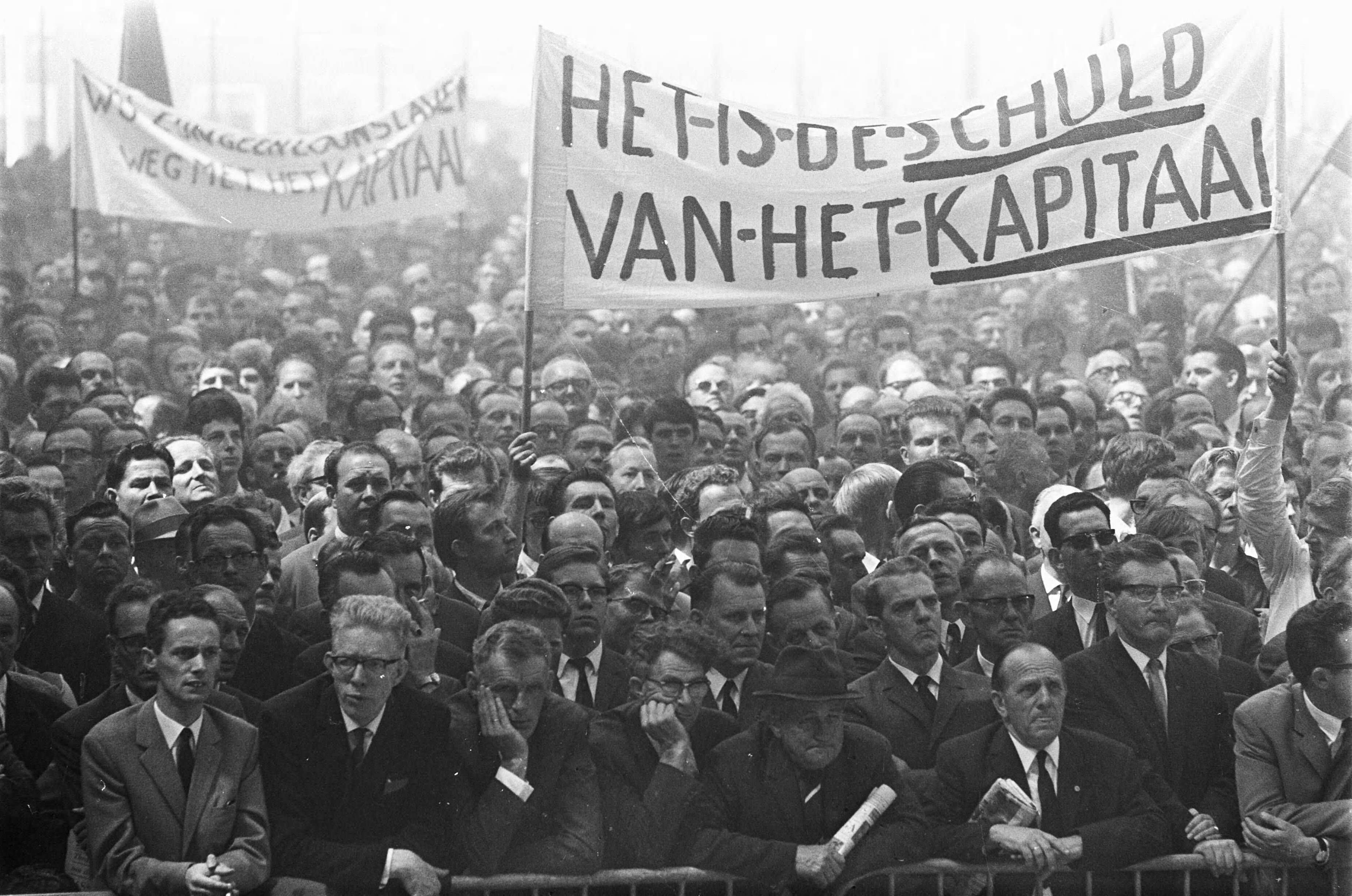 Fotocollectie Anefo — Vakbonden bijeen te Utrecht. Spandoek "Het is de schuld van het kapitaal" — Foto: Kroon, Ron / Anefo. Licentie: Set B: Rechtenvrij / Publiek Domein. Bron: Nationaal Archief. http://hdl.handle.net/10648/ab421d38-d0b4-102d-bcf8-003048976d84