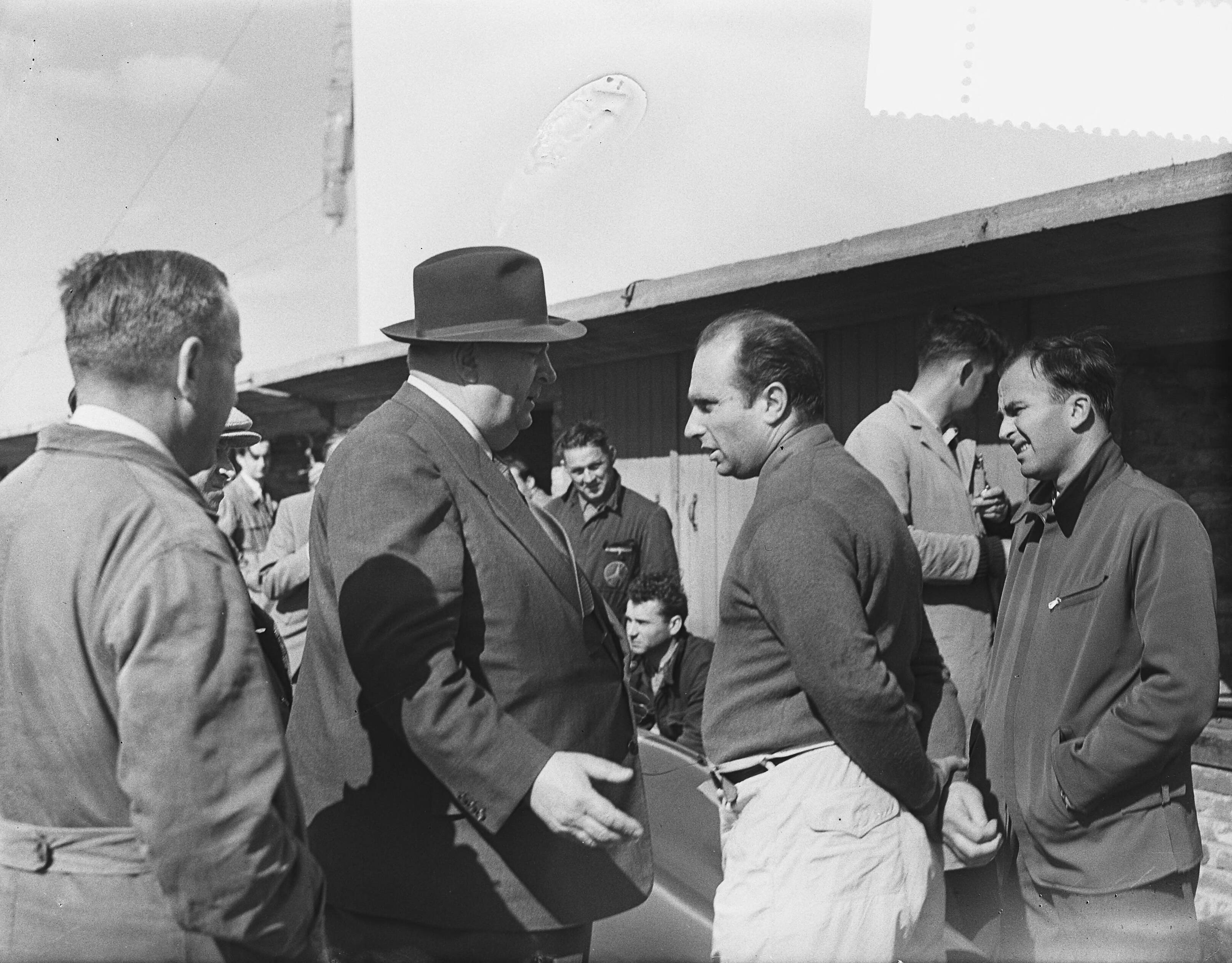 Fotocollectie Anefo — Training voor de Grote Prijs van Nederland op Zandvoort. Leider van de Mercedesploeg Alfred Neubauer (met hoed) in gesprek met de Argentijnse coureur Juan-Manuel Fangio — Foto: Bilsen, Joop van / Anefo. Licentie: Set B: Rechtenvrij / Publiek Domein. Bron: Nationaal Archief. http://hdl.handle.net/10648/a936bbb6-d0b4-102d-bcf8-003048976d84