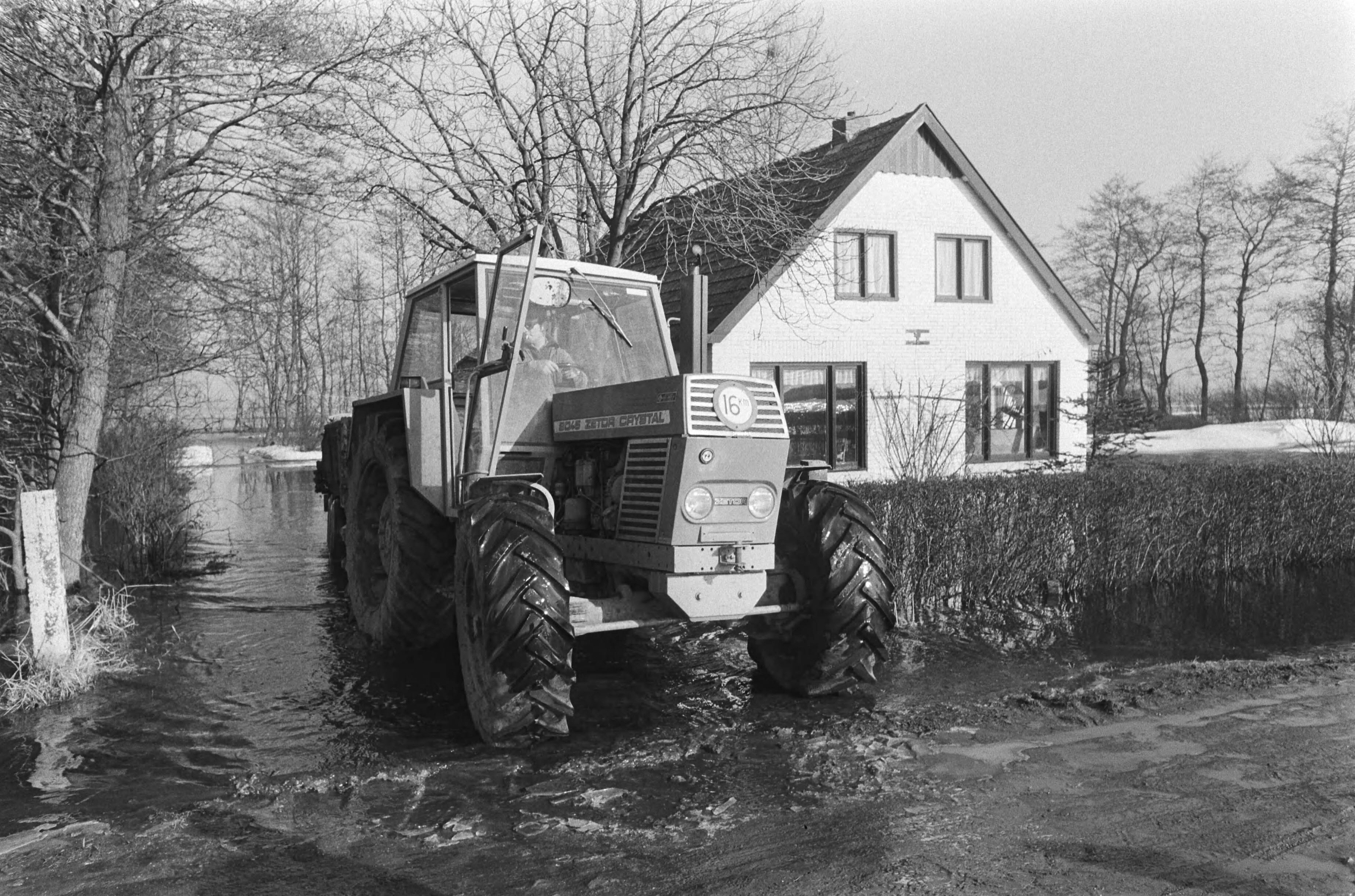 Wateroverlast in Groningen en Friesland — Tractor voor een woonhuis in het water — Foto: Suyk, Koen / Anefo. Licentie: Set B: Rechtenvrij / Publiek Domein. Bron: Nationaal Archief. http://hdl.handle.net/10648/acc59e96-d0b4-102d-bcf8-003048976d84