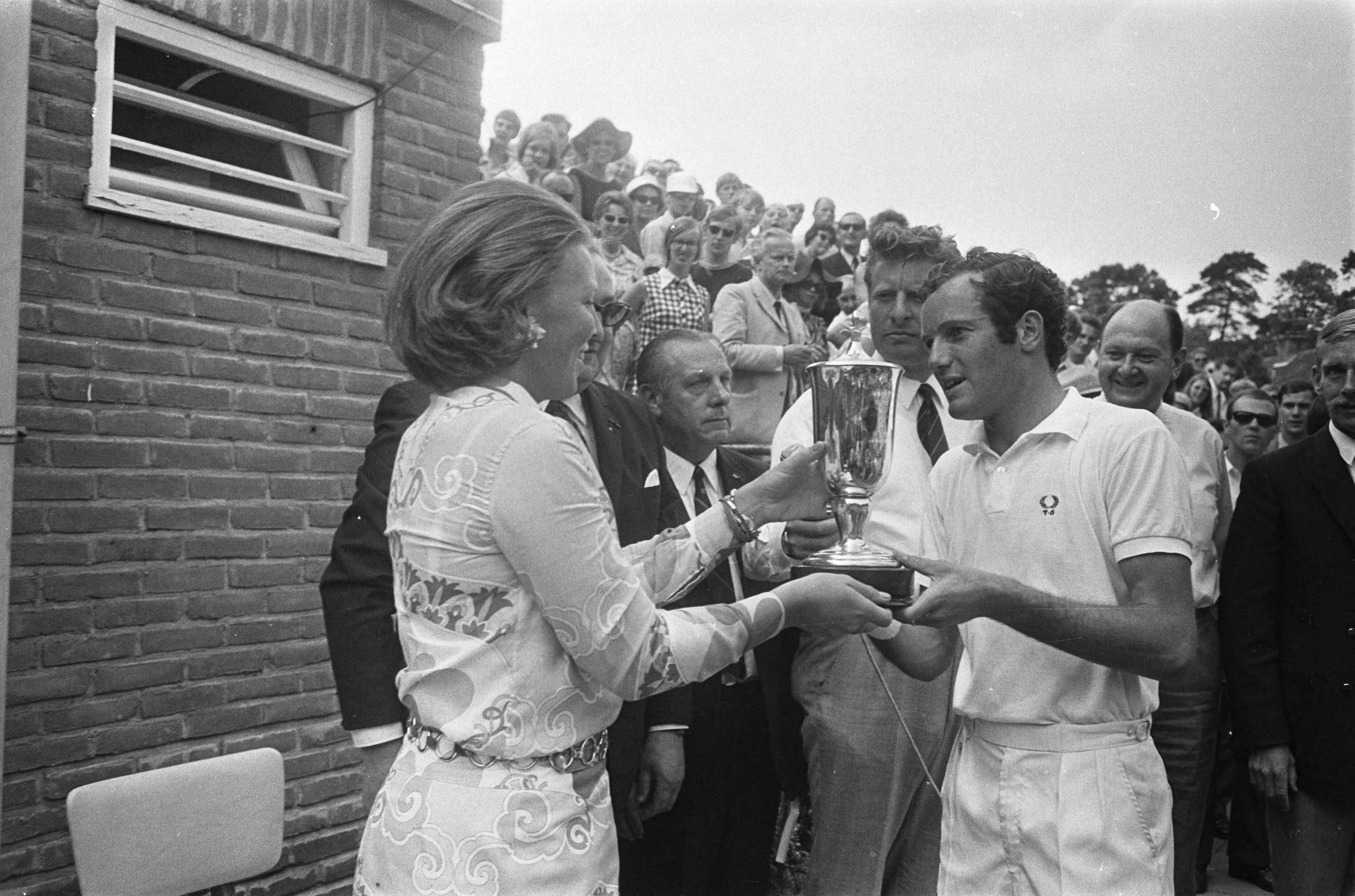 Fotocollectie Anefo — Internationaal tennistoernooi in Hilversum ( t Melkhuisje winnaar Tom Okker ontvangt beker van Prinses Beatrix — Foto: Koch, Eric / Anefo. Licentie: Set B: Rechtenvrij / Publiek Domein. Bron: Nationaal Archief. http://hdl.handle.net/10648/ab9e7c72-d0b4-102d-bcf8-003048976d84