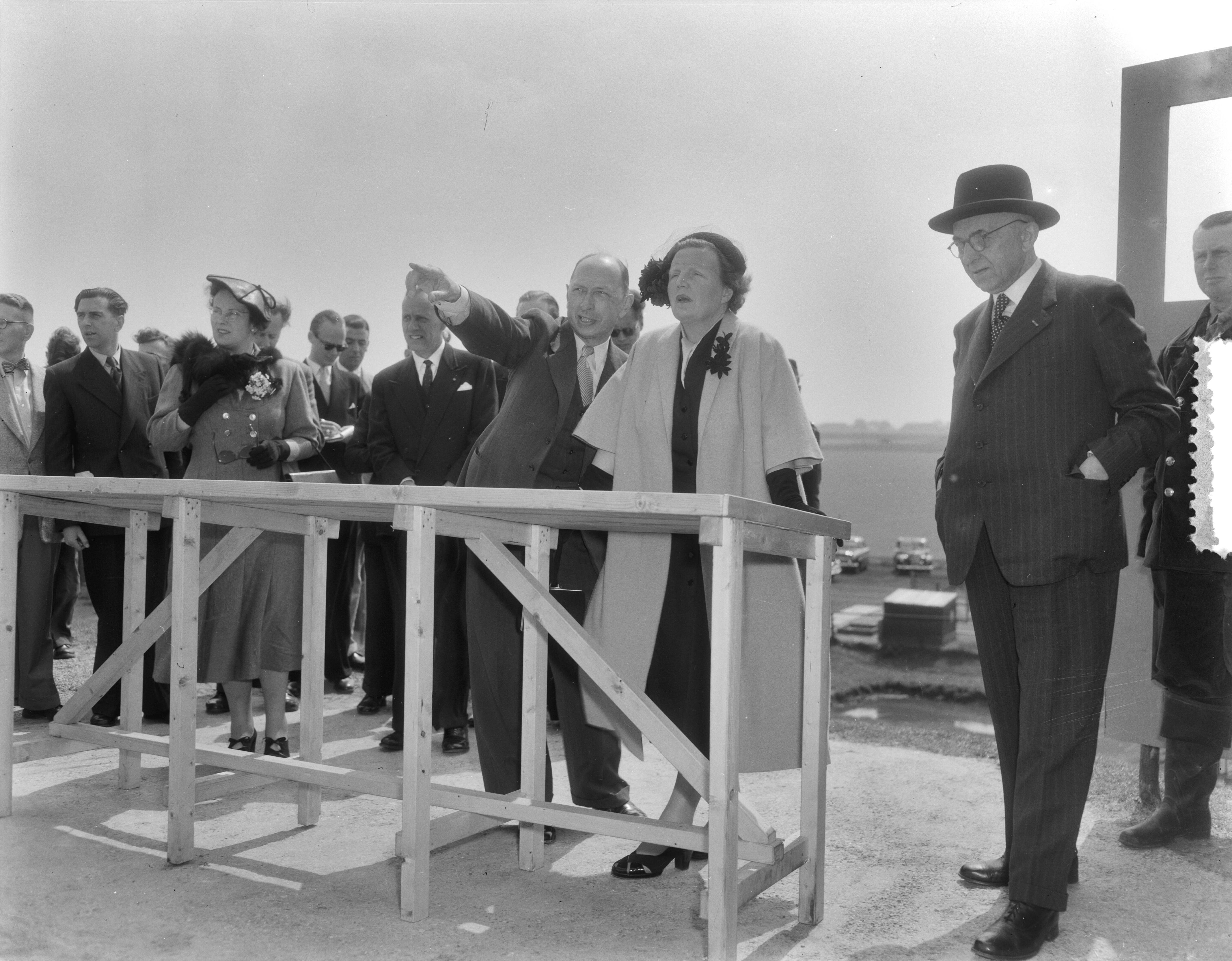 Werkbezoek van koningin Juliana aan de provincie Groningen (1954) — Werkbezoek van koningin Juliana aan de provincie Groningen. Op de zeedijk bij de Julianapolder, waar de koningin een uitzicht had over de Waddenzee en de landaanwinningswerken bekeek. Links van haar ir. W. Kooper, hoofdingenieur van Rijkswaterstaat en hoofd van de Dienst Landaanwinningswerken. In het midden de particuliere secretaresse van de koningin, mevr. Smitt-Avis — Foto: Duinen, G.W. van / Anefo. Licentie: Set B: Rechtenvrij / Publiek Domein. Bron: Nationaal Archief. http://hdl.handle.net/10648/a9229082-d0b4-102d-bcf8-003048976d84