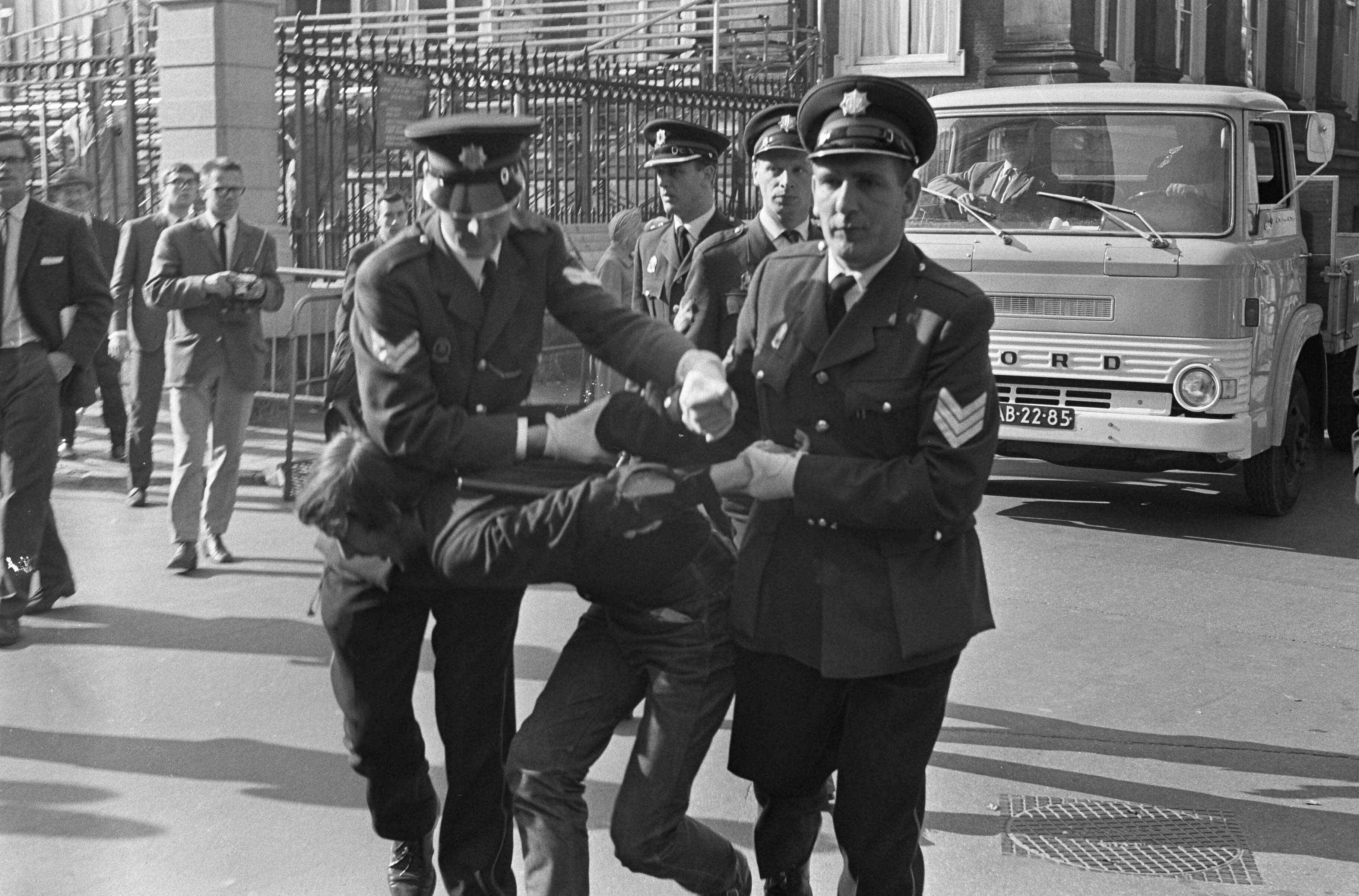 Protesterende Amsterdamse Provo's tijdens Prinsjesdag 1966 in Den Haag — Arrestatie van een lid van de Amsterdamse Provo — Foto: Fotograaf Onbekend / Anefo. Licentie: Set B: Rechtenvrij / Publiek Domein. Bron: Nationaal Archief. http://hdl.handle.net/10648/aafd42c6-d0b4-102d-bcf8-003048976d84