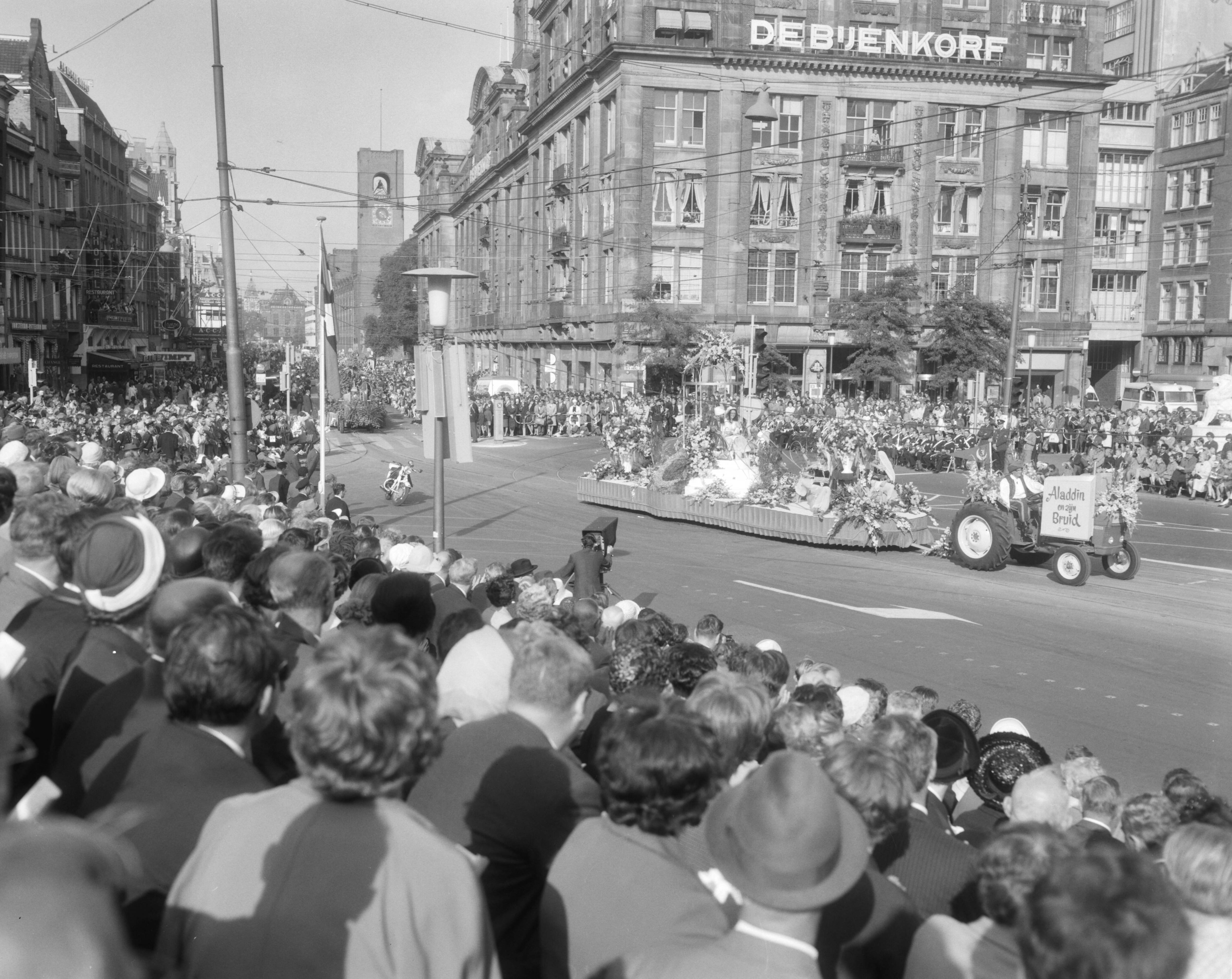 Bloemencorso van Aalsmeer te Amsterdam — Een praalwagen bij de Dam te Amsterdam met op de achtergrond het warenhuis de Bijenkorf — Foto: Bilsen, Joop van / Anefo. Licentie: Set B: Rechtenvrij / Publiek Domein. Bron: Nationaal Archief. http://hdl.handle.net/10648/aafaebc0-d0b4-102d-bcf8-003048976d84
