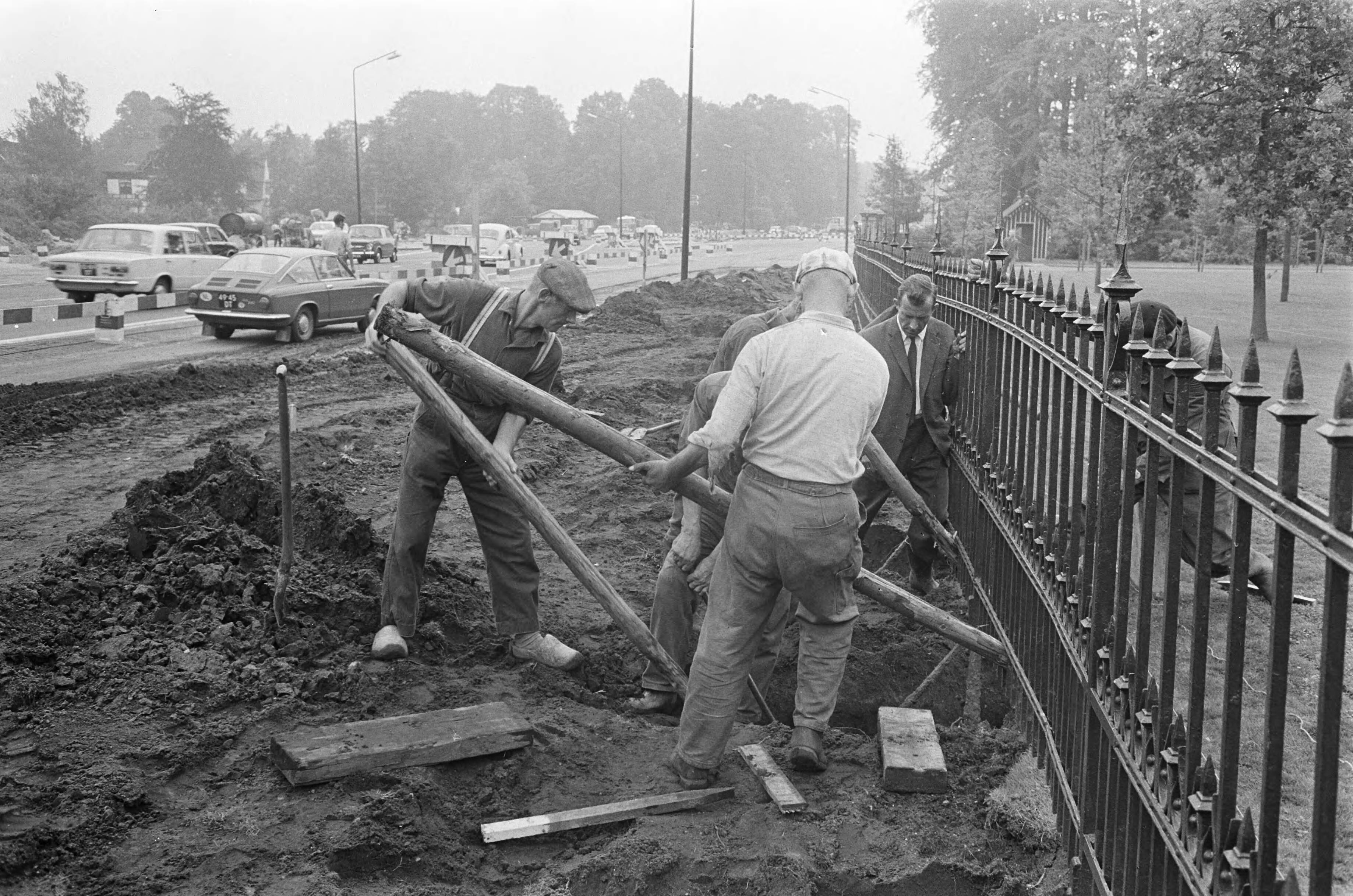 Aanleg van een vierbaansweg voor Paleis Soestdijk — Het opnieuw rechtzetten van het hek rond de paleistuin — Foto: Fotograaf Onbekend / Anefo. Licentie: Set B: Rechtenvrij / Publiek Domein. Bron: Nationaal Archief. http://hdl.handle.net/10648/ab496624-d0b4-102d-bcf8-003048976d84