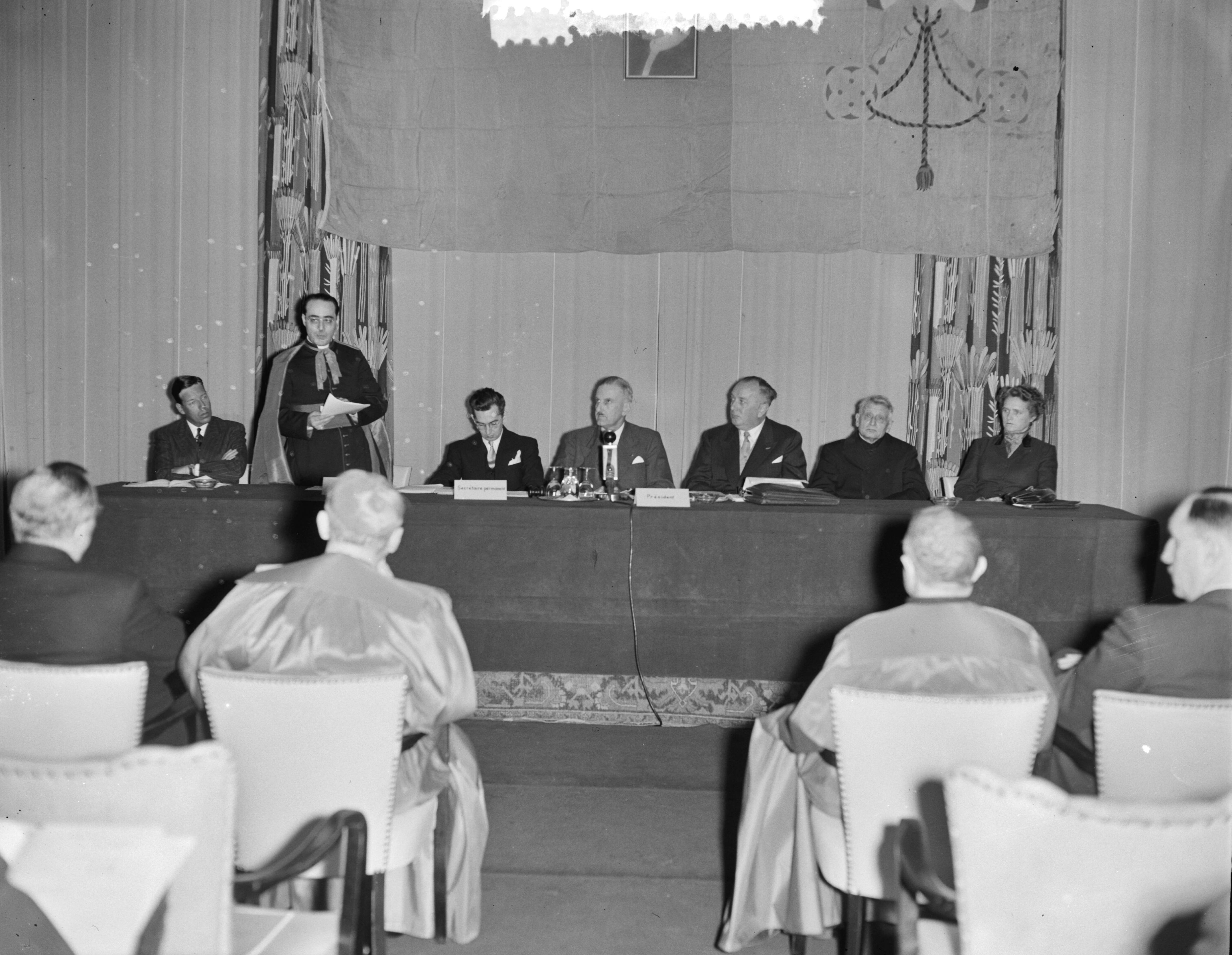 Fotocollectie Anefo — Congres van de Internationale Katholieke Werkgeversorganisaties in het Kurhaus te Scheveningen. Toespraak van een geestelijke — Foto: Pot, Harry / Anefo. Licentie: Set B: Rechtenvrij / Publiek Domein. Bron: Nationaal Archief. http://hdl.handle.net/10648/a931ebcc-d0b4-102d-bcf8-003048976d84