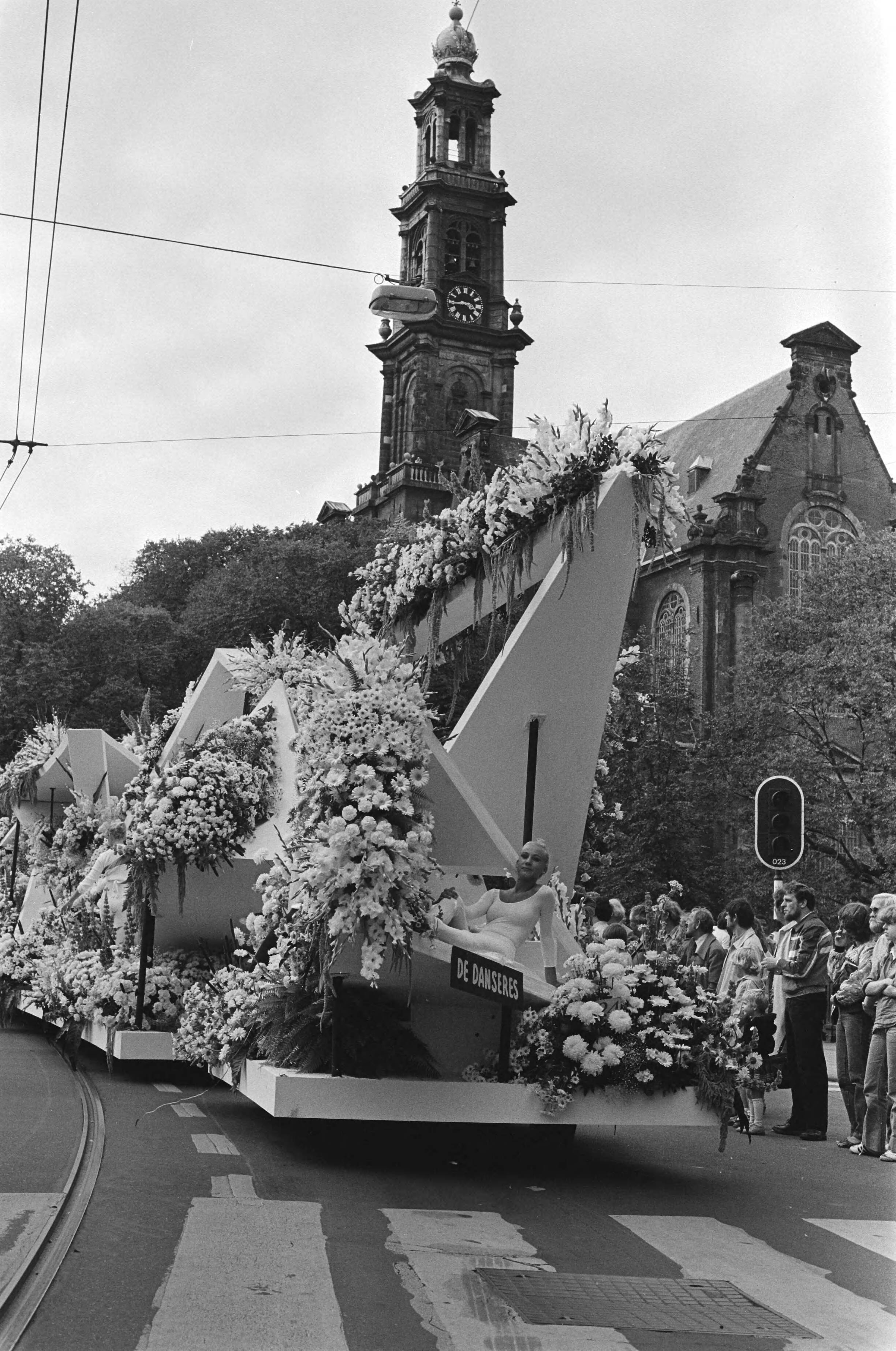 Aalsmeerse bloemencorso — Onder motto De bezige mens door Amsterdam; praalwagen De danseres passeert de Westertoren — Foto: Bogaerts, Rob / Anefo. Licentie: Set B: Rechtenvrij / Publiek Domein. Bron: Nationaal Archief. http://hdl.handle.net/10648/ace714ea-d0b4-102d-bcf8-003048976d84