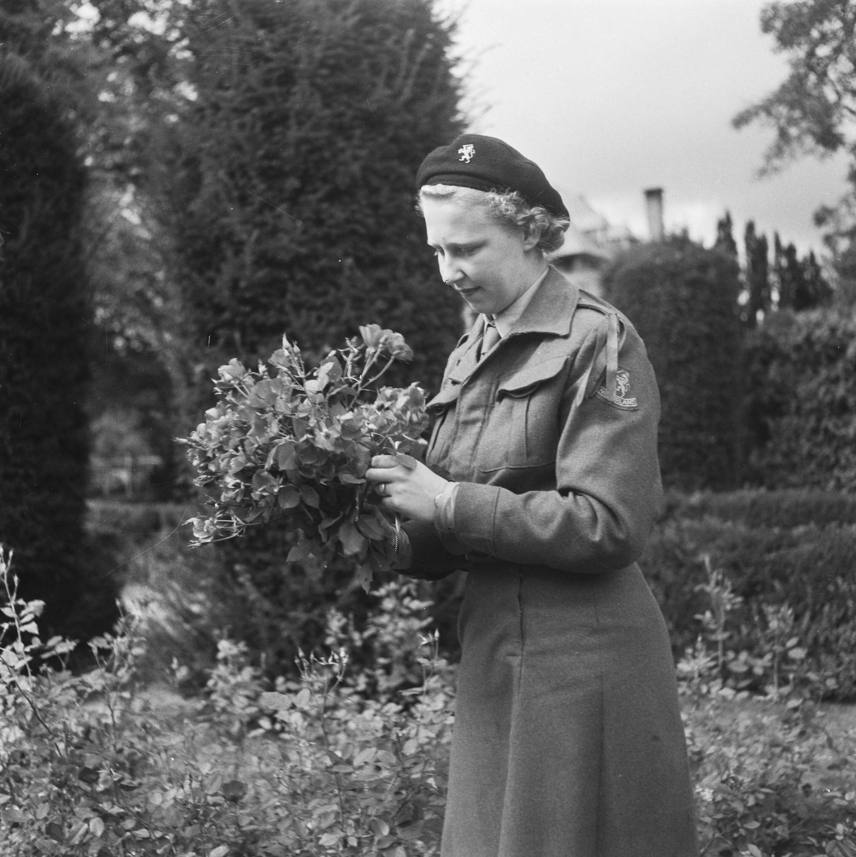 Opleidingskamp voor het Vrouwenhulpkorps te Bouvigne — [lid VHK met bloemen uit de tuin] — Foto: Fotograaf Onbekend / Anefo. Licentie: Set B: Rechtenvrij / Publiek Domein. Bron: Nationaal Archief. http://hdl.handle.net/10648/ac15e0aa-d0b4-102d-bcf8-003048976d84