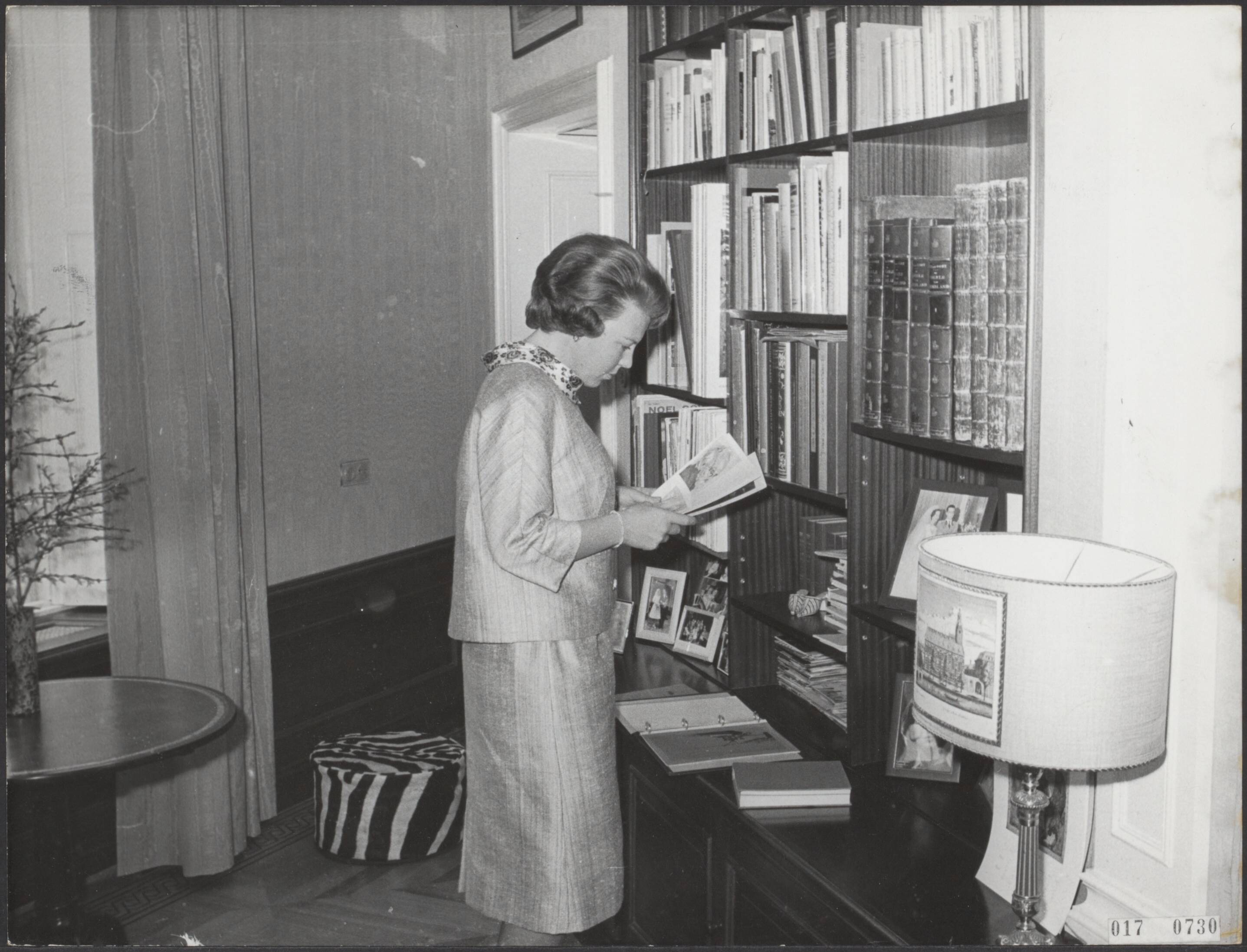 Fotocollectie Elsevier Binnenland — Serie: kasteel Drakensteyn bewoond door prinses Beatrix. Prinses Beatrix bekijkt een brochure staande voor een boekenkast — Foto: ANP / RVD of rechtenvrij. Licentie: Set B: Rechtenvrij / Publiek Domein. Bron: Nationaal Archief. http://hdl.handle.net/10648/adbed36c-d0b4-102d-bcf8-003048976d84