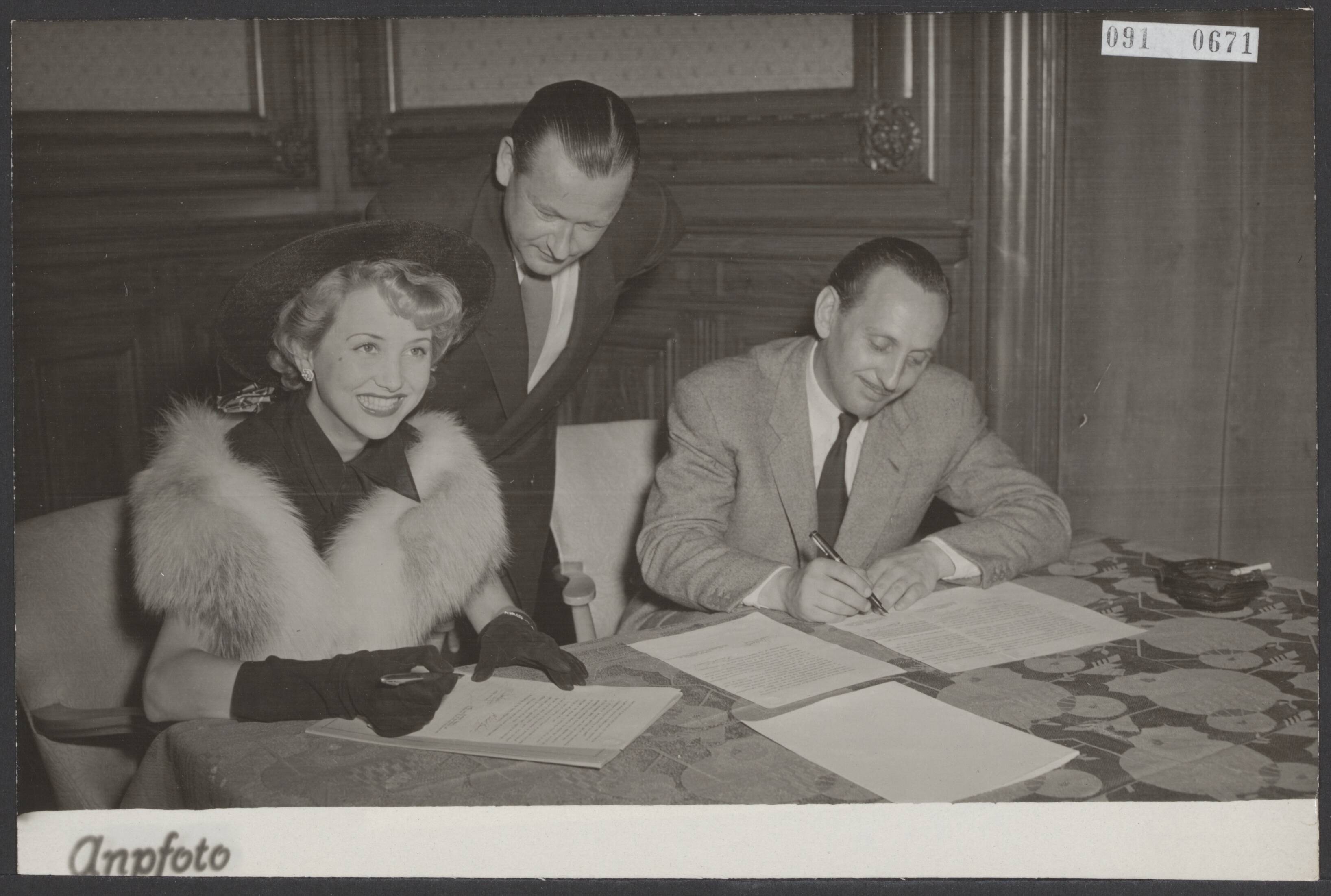Fotocollectie Elsevier Binnenland — Mannequin tekent filmcontract. In het Palace Hotel te Scheveningen tekende de Rotterdamse mannequin Annika van Kooy het filmcontract dat haar in staat stelt naar Hollywood te gaan, alwaar zij een vooropleiding zal krijgen om daarna te gaan filmen in Europa. Tijdens het tekenen van het contract. Naast Annika van Kooy Michael Howard. Achter haar haar advocaat mr. F. Hartong — Foto: ANP / RVD of rechtenvrij. Licentie: Set B: Rechtenvrij / Publiek Domein. Bron: Nationaal Archief. http://hdl.handle.net/10648/ae20a722-d0b4-102d-bcf8-003048976d84
