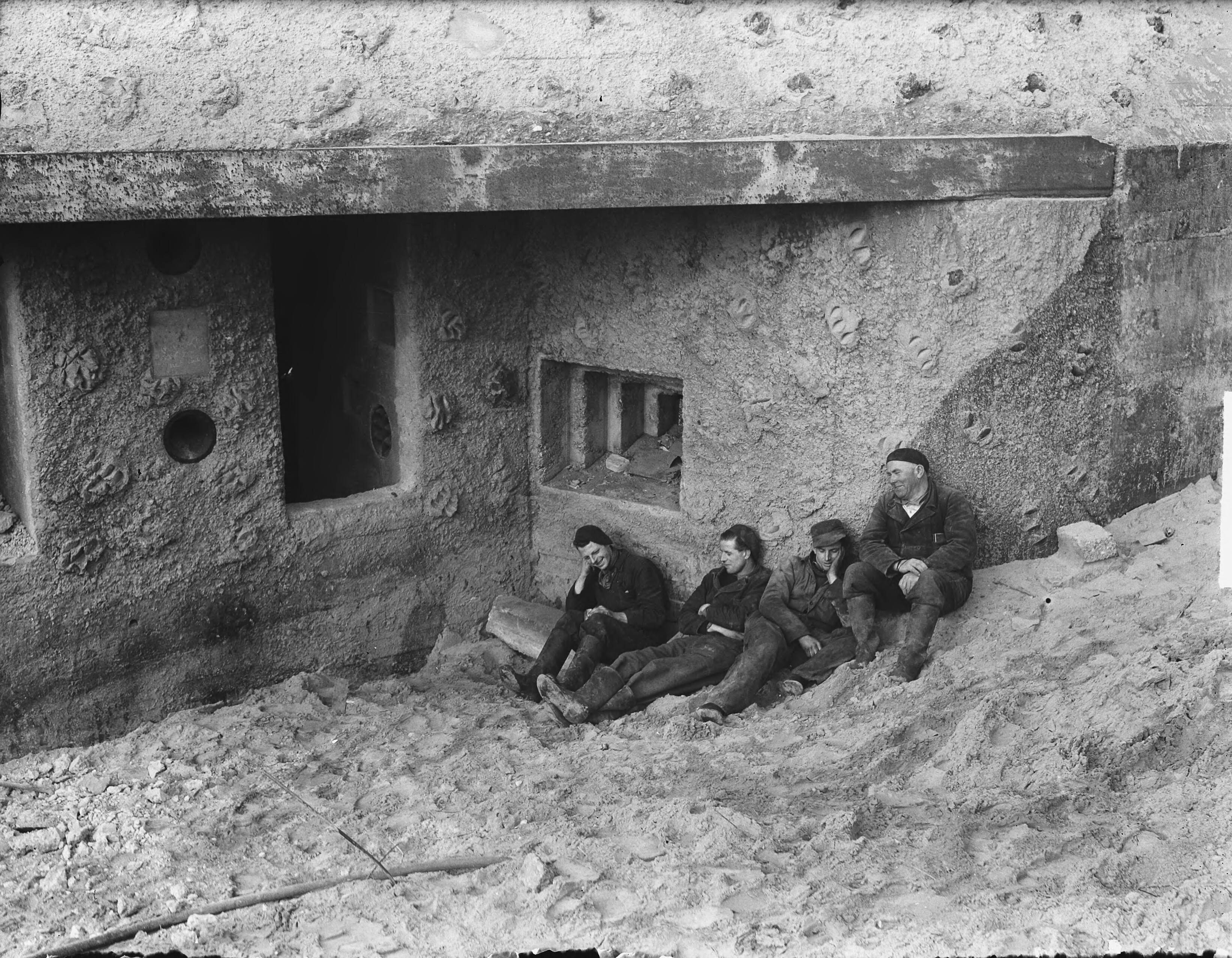 Arbeiders pauzeren in de zon tijdens de sloop van bunkers te Zandvoort — Foto: Vogel, Carel L. de / Anefo. — Licentie: Set B: Rechtenvrij / Publiek Domein. Bron: Nationaal Archief. http://hdl.handle.net/10648/a8e5bd9c-d0b4-102d-bcf8-003048976d84