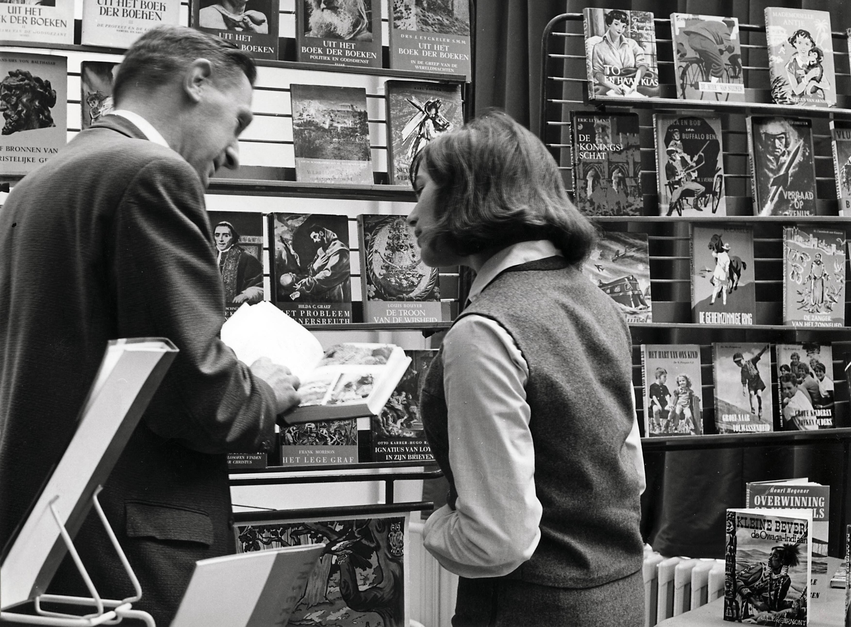 Collectie nader te bepalen — [Serie: Drukkerij N.V. Spaarnestad] Personeelsbibliotheek. Dhr. de Vré toont het boek "Portret van Portugal" aan Leni Hei van de markanalyse — Foto: Boer, F. de / Spaarnestad Photo (05887). Licentie: Set B: Rechtenvrij / Publiek Domein. Bron: Nationaal Archief. http://hdl.handle.net/10648/35429da6-3f8a-a382-e063-6df0900a6686