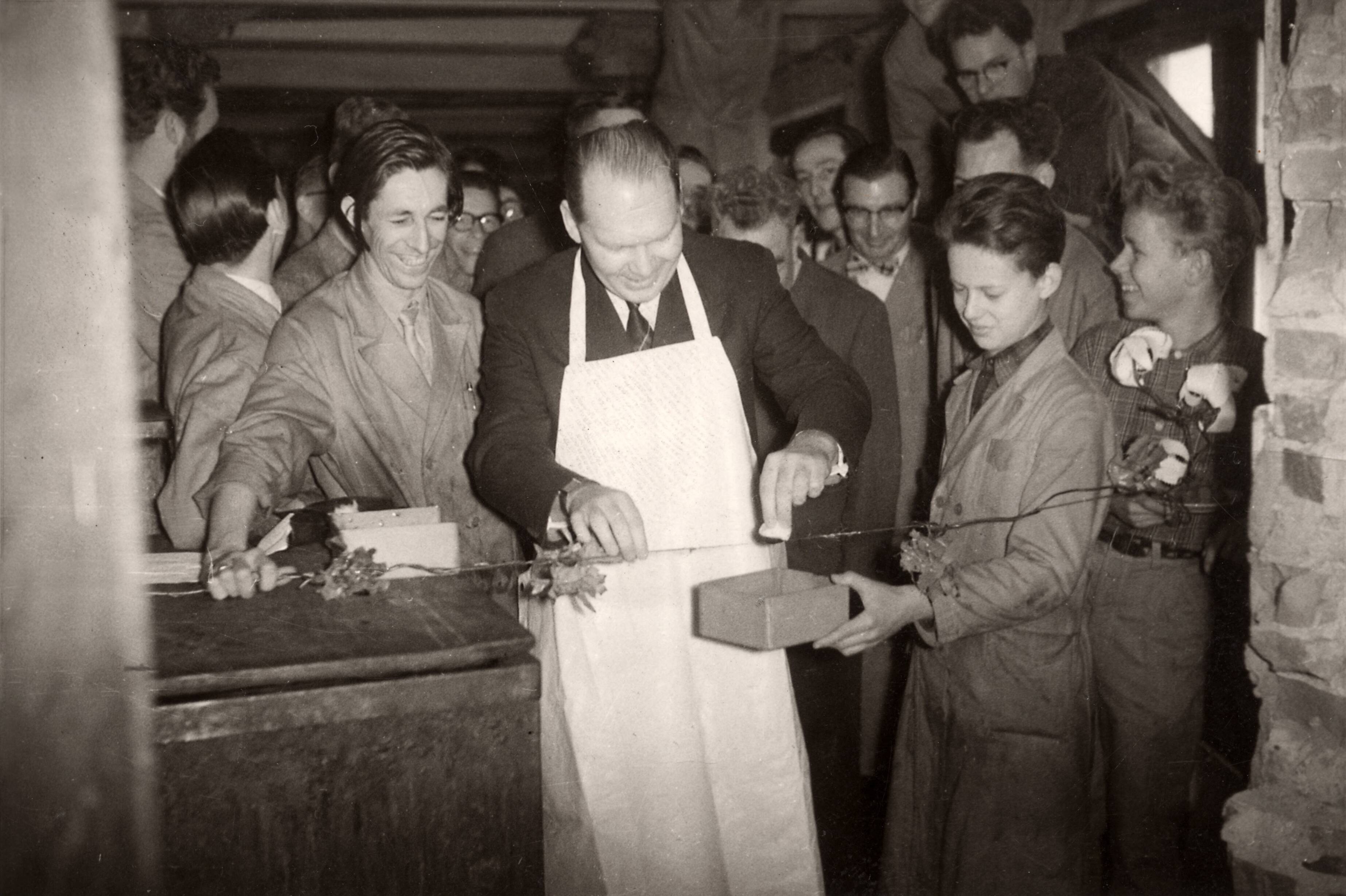 Collectie nader te bepalen — [Serie: Bedrijfsvoering Spaarnestad][man met schort verricht een openingsplechtigheid door het schuren over een draad, om hem heen mannen in stofjassen] — Foto: Fotograaf Onbekend / Fotobureau onbekend / Spaarnestad Photo (05887). Licentie: Set B: Rechtenvrij / Publiek Domein. Bron: Nationaal Archief. http://hdl.handle.net/10648/35429da6-4262-a382-e063-6df0900a6686