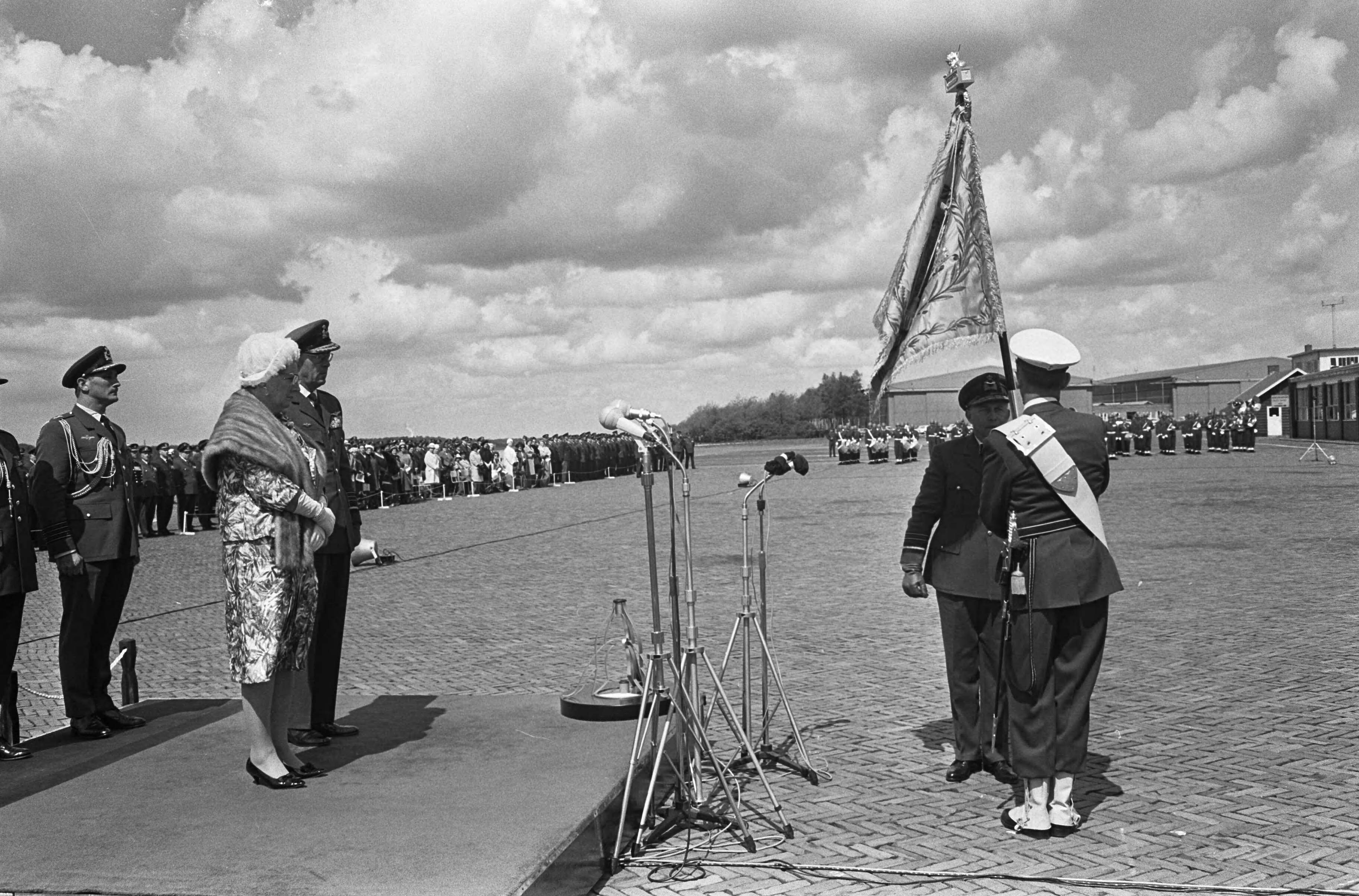 Fotocollectie Anefo — Koningin Juliana geeft vaandel aan de Koninklijke Luchtmacht, koningin Juliana en prins Berhard op podium, rechts de vaandeldrager — Foto: Koch, Eric / Anefo. Licentie: Set B: Rechtenvrij / Publiek Domein. Bron: Nationaal Archief. http://hdl.handle.net/10648/aaa95418-d0b4-102d-bcf8-003048976d84