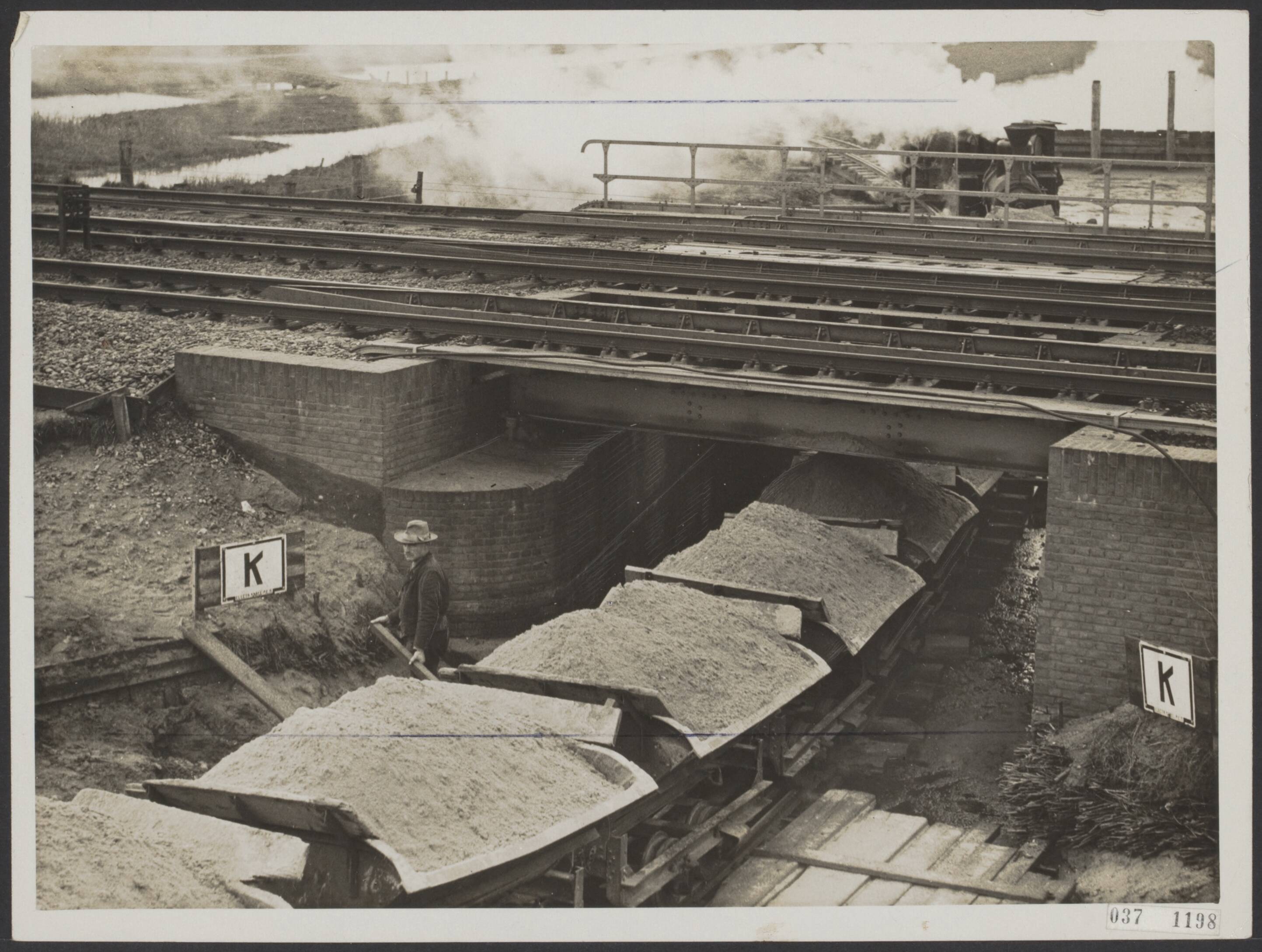 Fotocollectie Elsevier Binnenland — Aanleg van de primaire weg Amsterdam-Alkmaar even achter het station Zaandam. In verband met het zandtransport nodig voor de aanleg van deze weg heeft men het kanaaltje dat onder de spoorbaan doorliep gedempt en hiervoor in de plaats de rails voor het zandtreintje gelegd — Foto: N.V. Polygoon. Licentie: Set B: Rechtenvrij / Publiek Domein. Bron: Nationaal Archief. http://hdl.handle.net/10648/adefd232-d0b4-102d-bcf8-003048976d84