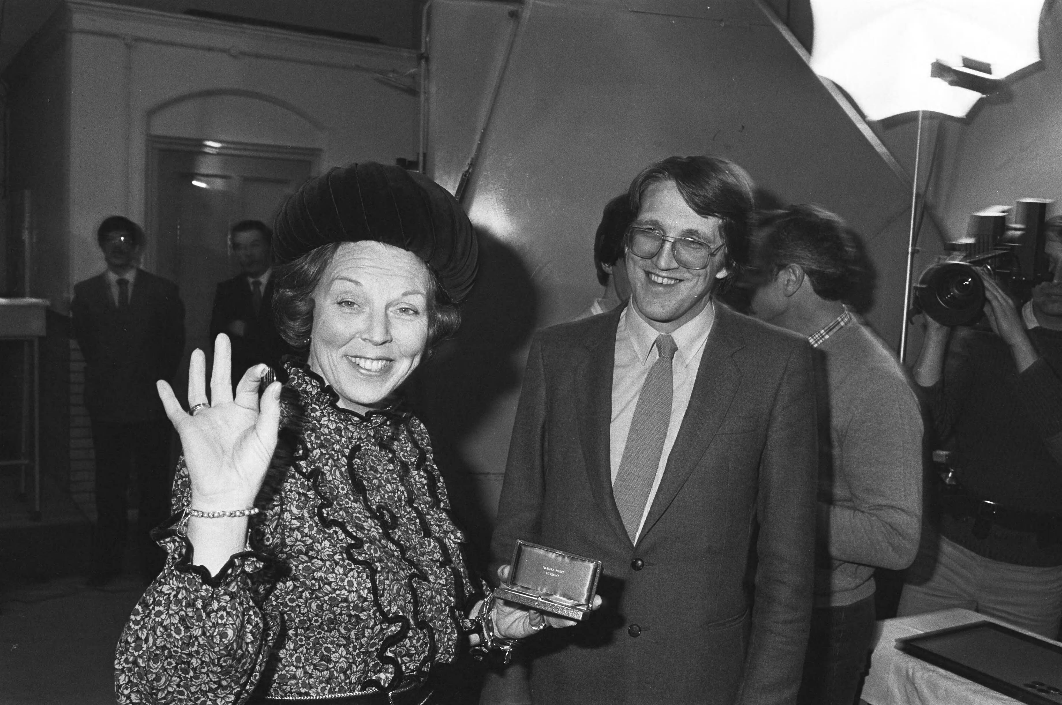 Fotocollectie Anefo — Beatrix slaat ook eerste nieuwe guldens in Rijksmunt te Utrecht laat de eerste nieuwe geslagen munt zien, staatssecretaris Kombrink van Financien / — Foto: Antonisse, Marcel / Anefo. Licentie: Set B: Rechtenvrij / Publiek Domein. Bron: Nationaal Archief. http://hdl.handle.net/10648/ad0d6014-d0b4-102d-bcf8-003048976d84
