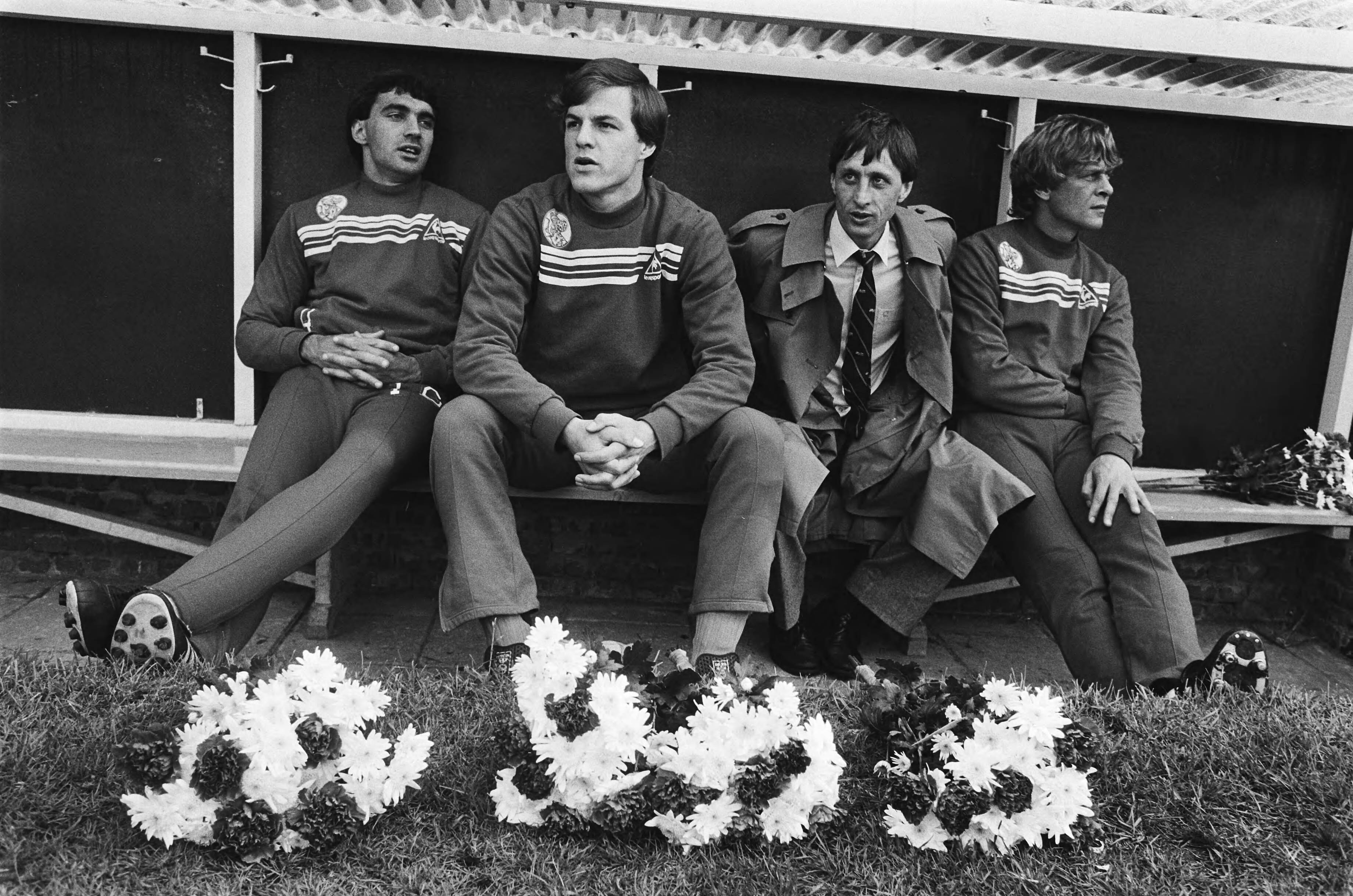 Fotocollectie Anefo — Voetbal Haarlem tegen Ajax 1-3; Johan Cruijff in regenjas tussen reservespelers op bankje, op voorgrond bloemen — Foto: Bogaerts, Rob / Anefo. Licentie: Set B: Rechtenvrij / Publiek Domein. Bron: Nationaal Archief. http://hdl.handle.net/10648/ad182008-d0b4-102d-bcf8-003048976d84