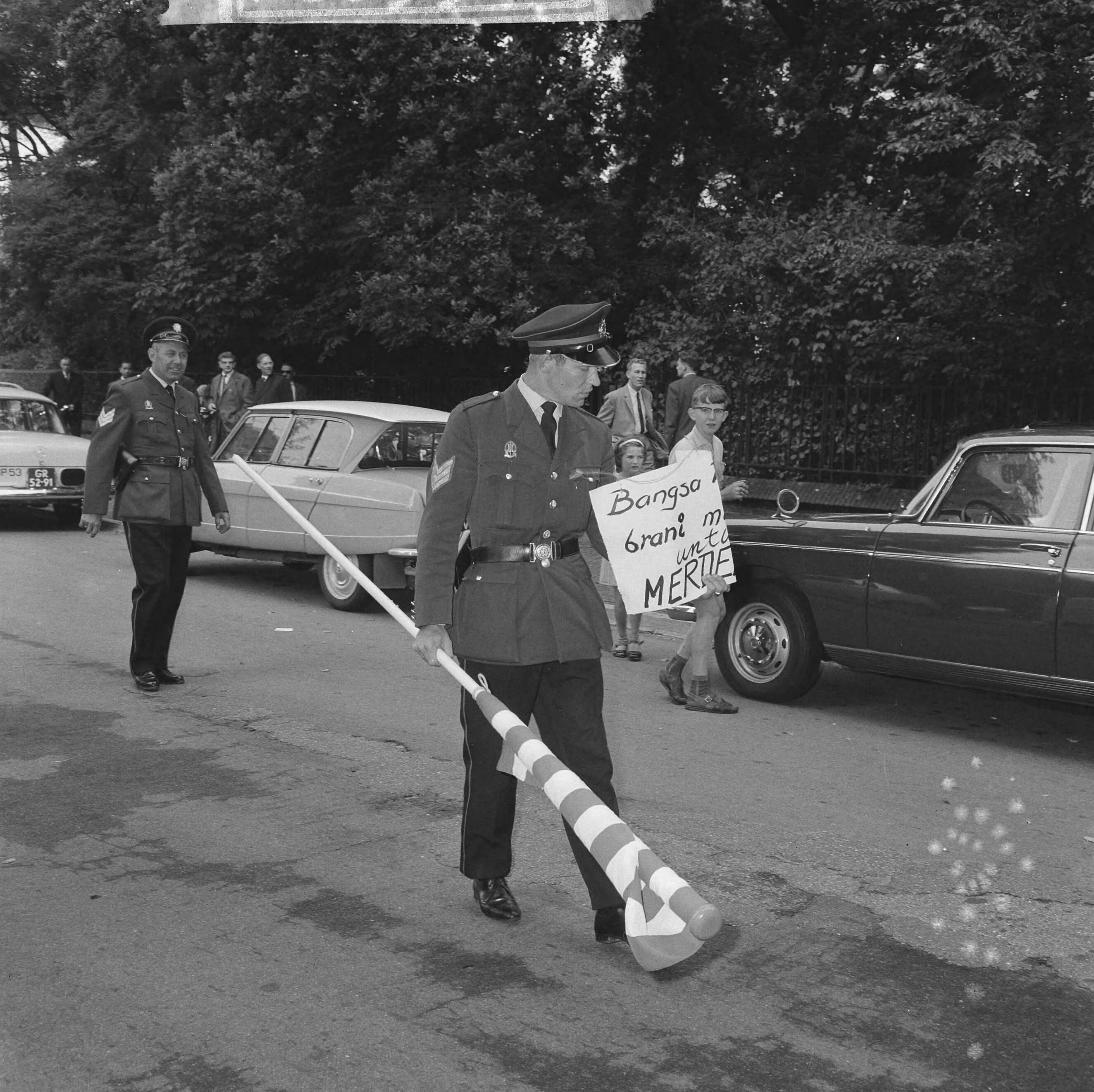 Fotocollectie Anefo — Papoea's demonstreren in Den Haag, een agent met een vlag en een protestbord — Foto: Nijs, Jac. de / Anefo. Licentie: Set B: Rechtenvrij / Publiek Domein. Bron: Nationaal Archief. http://hdl.handle.net/10648/aabc69f4-d0b4-102d-bcf8-003048976d84