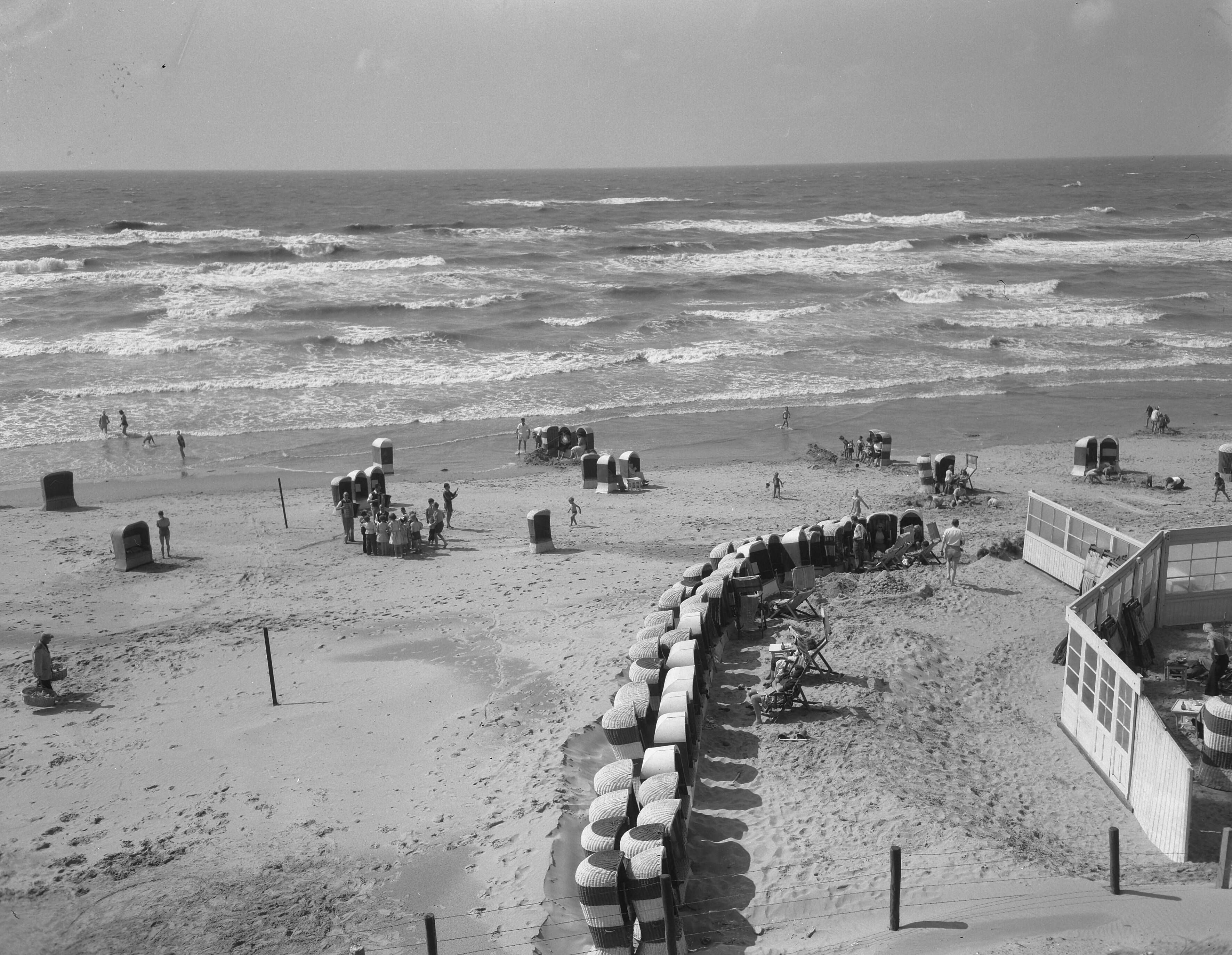 Fotocollectie Anefo — Zandvoort. Slecht strandweer. Strandstoelen staan in een cirkel opsteld bij een strandpaviloen als bescherming tegen wind — Foto: Noske, J.D. / Anefo. Licentie: Set B: Rechtenvrij / Publiek Domein. Bron: Nationaal Archief. http://hdl.handle.net/10648/a9271c1a-d0b4-102d-bcf8-003048976d84