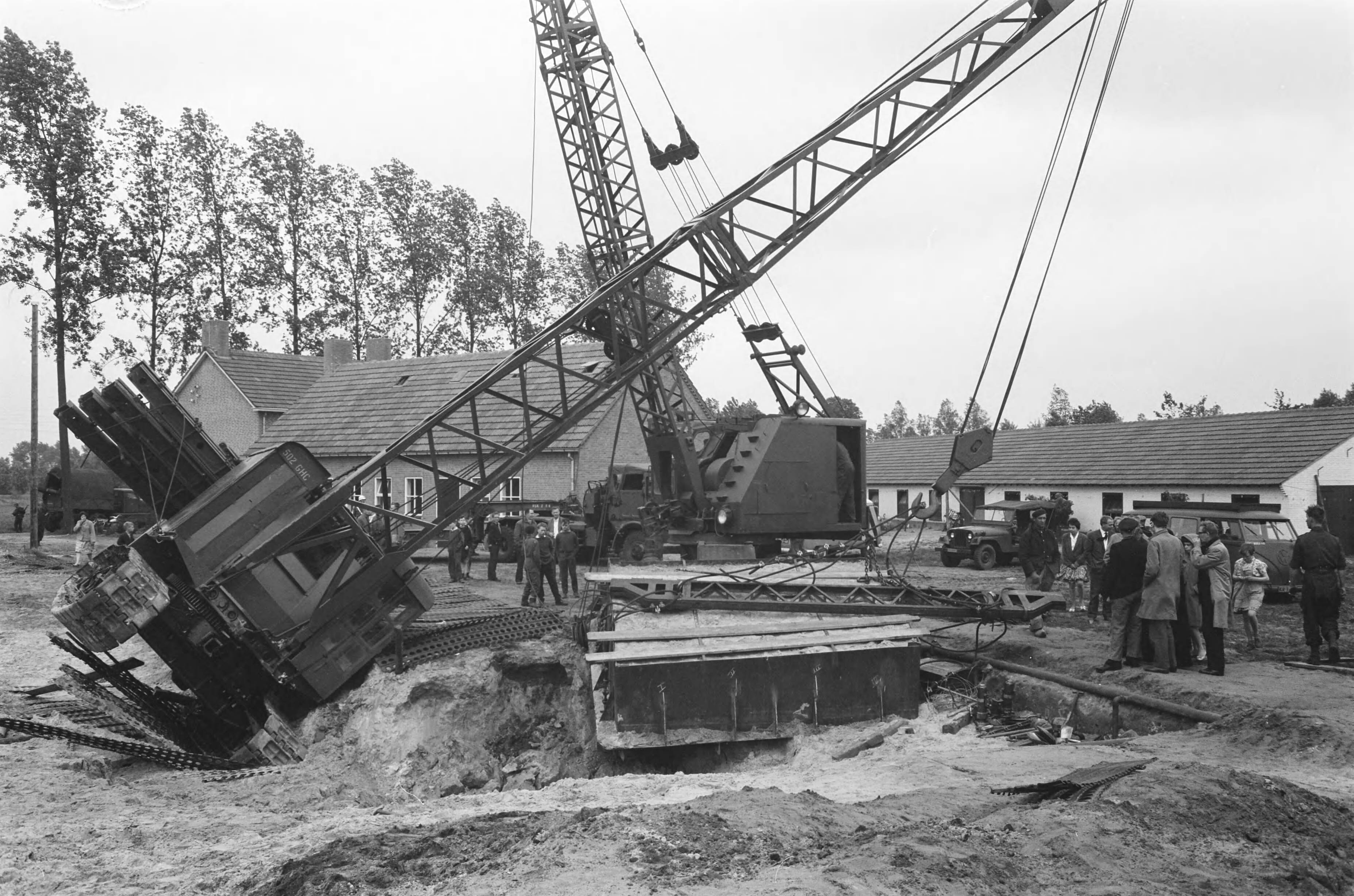 Fotocollectie Anefo — In Esch (N.B.) zijn militairen van het depot Genietroepen van de Koning Willem I-kazerne in Den Bosch bezig geweest met het uitgraven van een Romeins graf uit het begin van onze jaartelling. Het graf werd in een metalen bekisting gebouwd om in zijn geheel naar Amersfoort te worden overgebracht, waar de Rijksdienst voor Oudheidkundig Bodemonderzoek het zal bestuderen. Gisteren wilden twee kranen het graf op een vrachtauto tillen; een van de kranen kantelde echter. Het graf bleef ongedeerd — Foto: Pot, Harry / Anefo. Licentie: Set B: Rechtenvrij / Publiek Domein. Bron: Nationaal Archief. http://hdl.handle.net/10648/a9d66792-d0b4-102d-bcf8-003048976d84