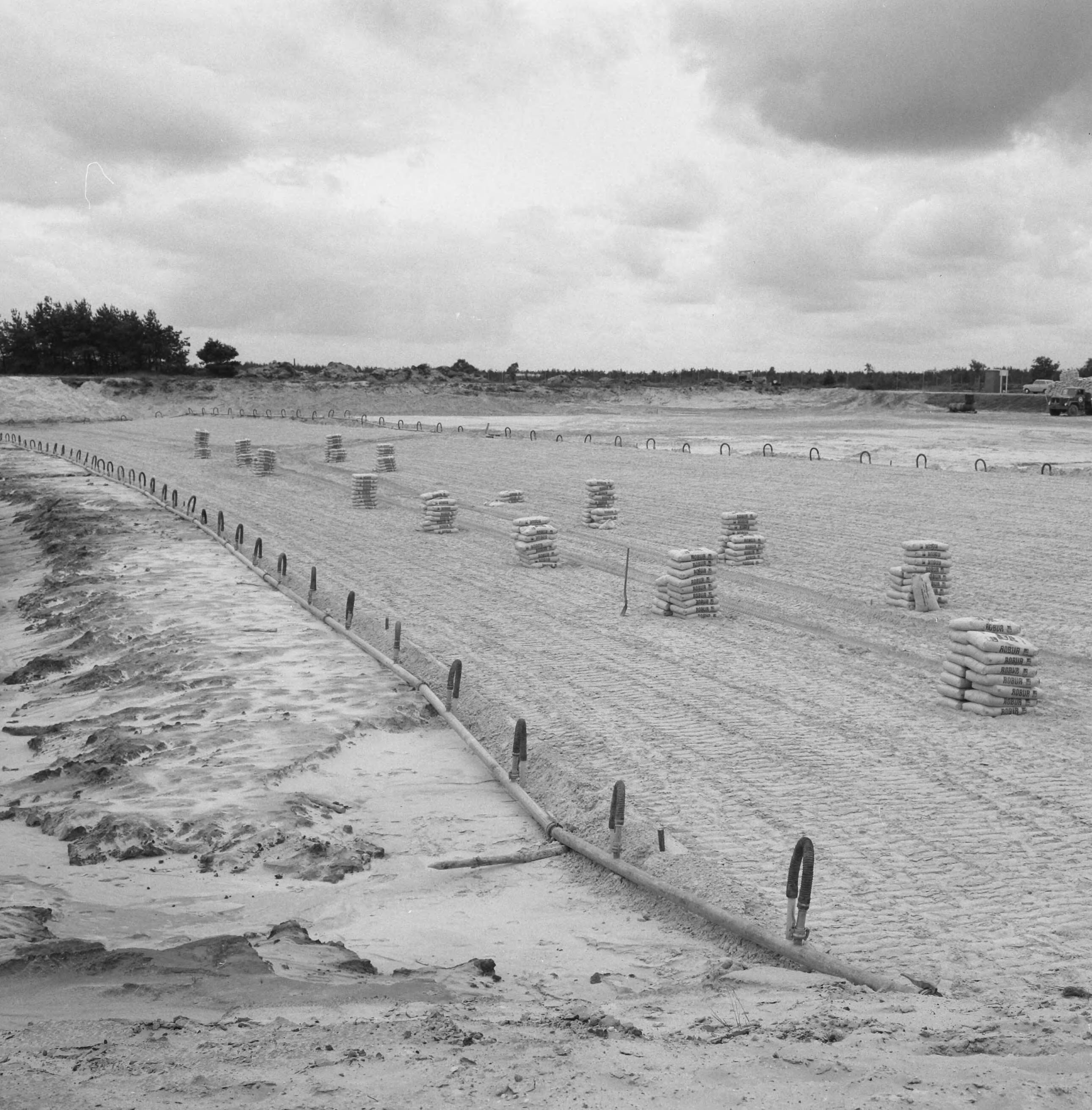 Fotocollectie Nederlandse Heidemaatschappij — Strandbad "Beekse Bergen". Overzicht van het werkterrein, gedeeltelijk gelegen onder de toekomstige waterlijn. Hierdoor werd het gebruik van bronbemaling noodzakelijk. De eerst vracht cement is aangevoerd — Foto: Wüllschleger, [...] / Heidemij. Licentie: Set B: Rechtenvrij / Publiek Domein. Bron: Nationaal Archief. http://hdl.handle.net/10648/ae85170c-d0b4-102d-bcf8-003048976d84