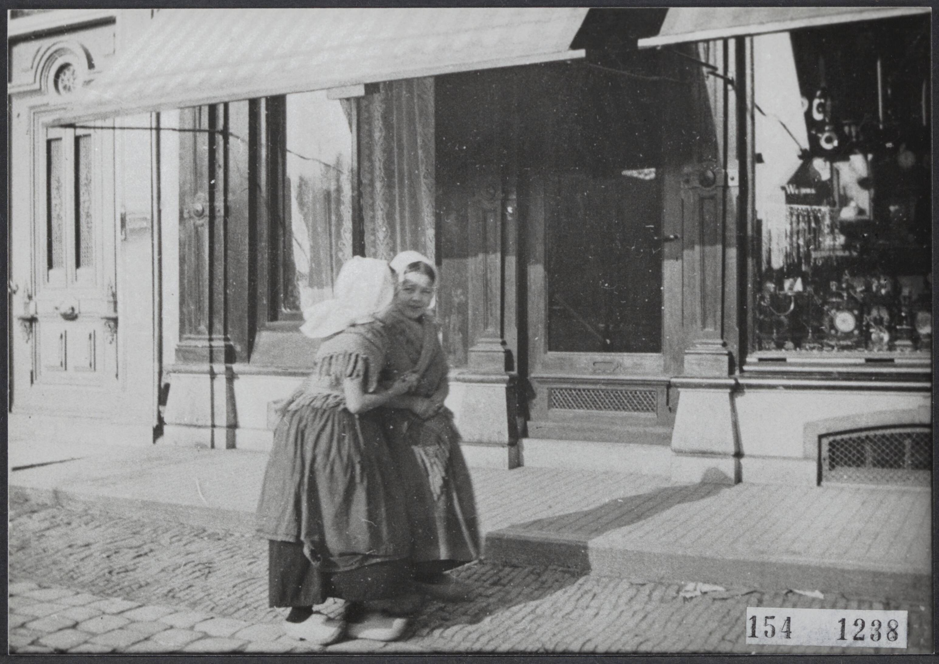 Serie Vanneufville (fotograaf uit Tourcoing 1855-1938) — Twee meisjes in klederdracht voor een winkel in Vlissingen — Foto: Vanneufville, Leonce Bertile. Licentie: Set B: Rechtenvrij / Publiek Domein. Bron: Nationaal Archief. http://hdl.handle.net/10648/ebbb0f04-fd5a-b173-dddc-14d9bd4f7fa0
