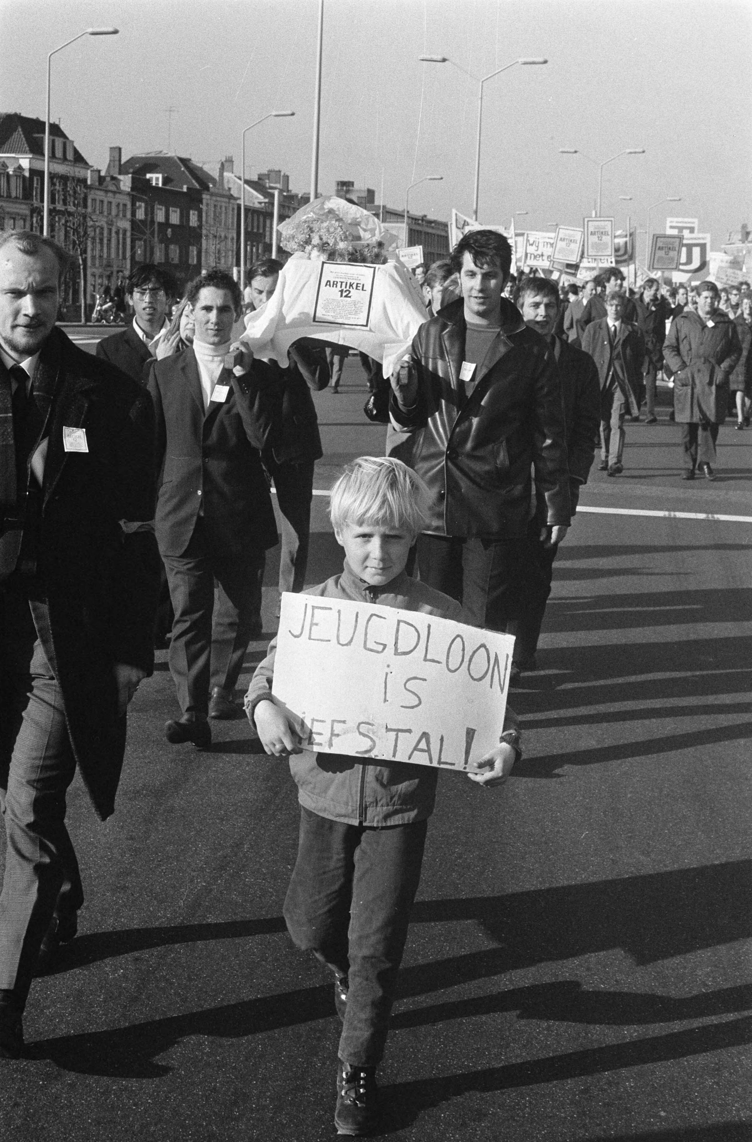 Fotocollectie Anefo — Demonstratie van Werkende Jongeren in Den Haag . Vooraan de stoet doodskist met artikel 12 — Foto: Verhoeff, Bert / Anefo. Licentie: Set B: Rechtenvrij / Publiek Domein. Bron: Nationaal Archief. http://hdl.handle.net/10648/ab7fa82e-d0b4-102d-bcf8-003048976d84