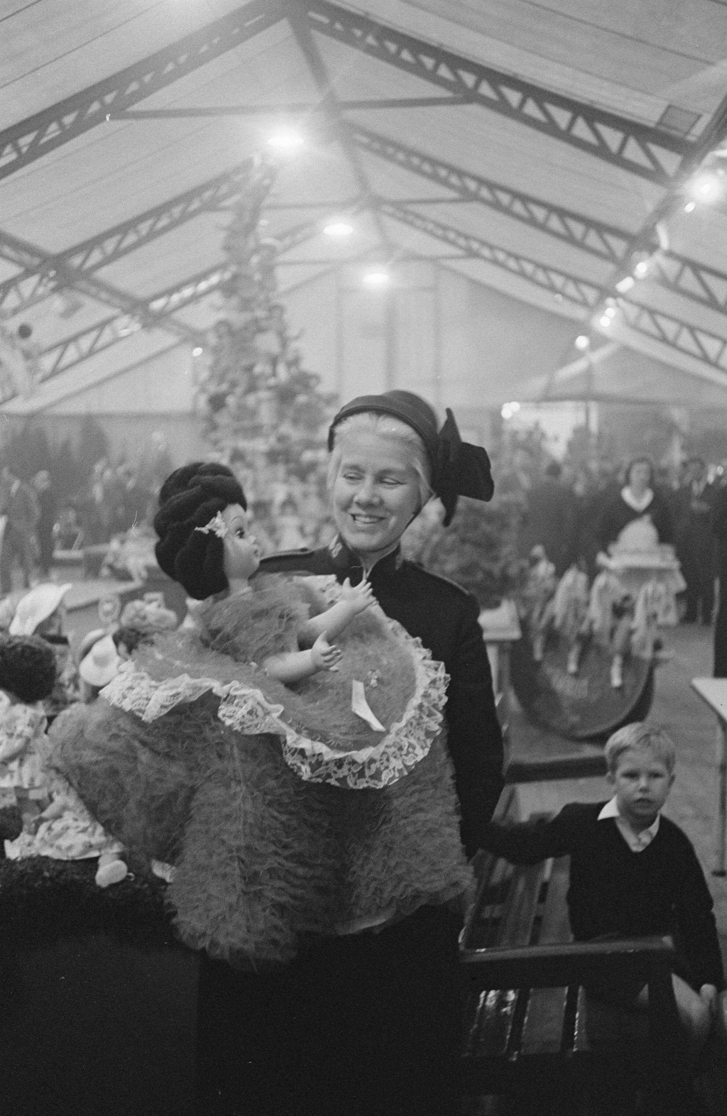 Fotocollectie Anefo — Albert Heijn N.V. in Zaandam heeft t.g.v. het 75-jarig bestaan aan haar vrienden en relaties gevraagd poppen te schenken i.p.v. de gebruikelijke cadeaus. Tijdens een receptie in Zaandam heeft de directie de poppen aan het Leger des Heils aangeboden. Luitenant-kolonel mej. M.E. Crok, secretaresse maatschappelijk werk van het Leger des Heils met een van de poppen — Foto: Pot, Harry / Anefo. Licentie: Set B: Rechtenvrij / Publiek Domein. Bron: Nationaal Archief. http://hdl.handle.net/10648/aa0a24e2-d0b4-102d-bcf8-003048976d84