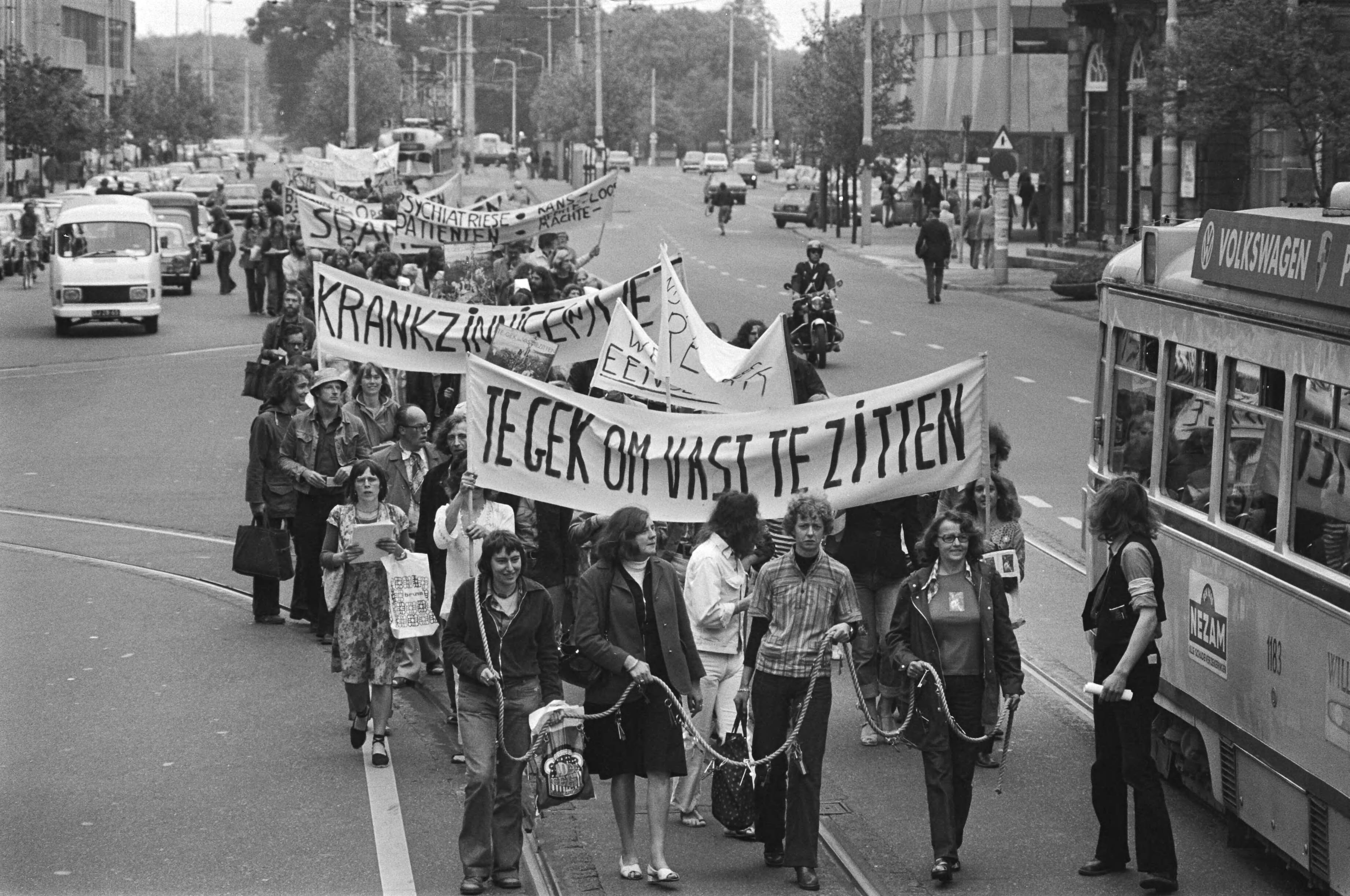 Fotocollectie Anefo — Demonstratie tegen krankzinnigheidswet " te gek om vast te zitten " in Den Haag , aan touwen gebonden demonstranten — Foto: Verhoeff, Bert / Anefo. Licentie: Set B: Rechtenvrij / Publiek Domein. Bron: Nationaal Archief. http://hdl.handle.net/10648/ac849aea-d0b4-102d-bcf8-003048976d84