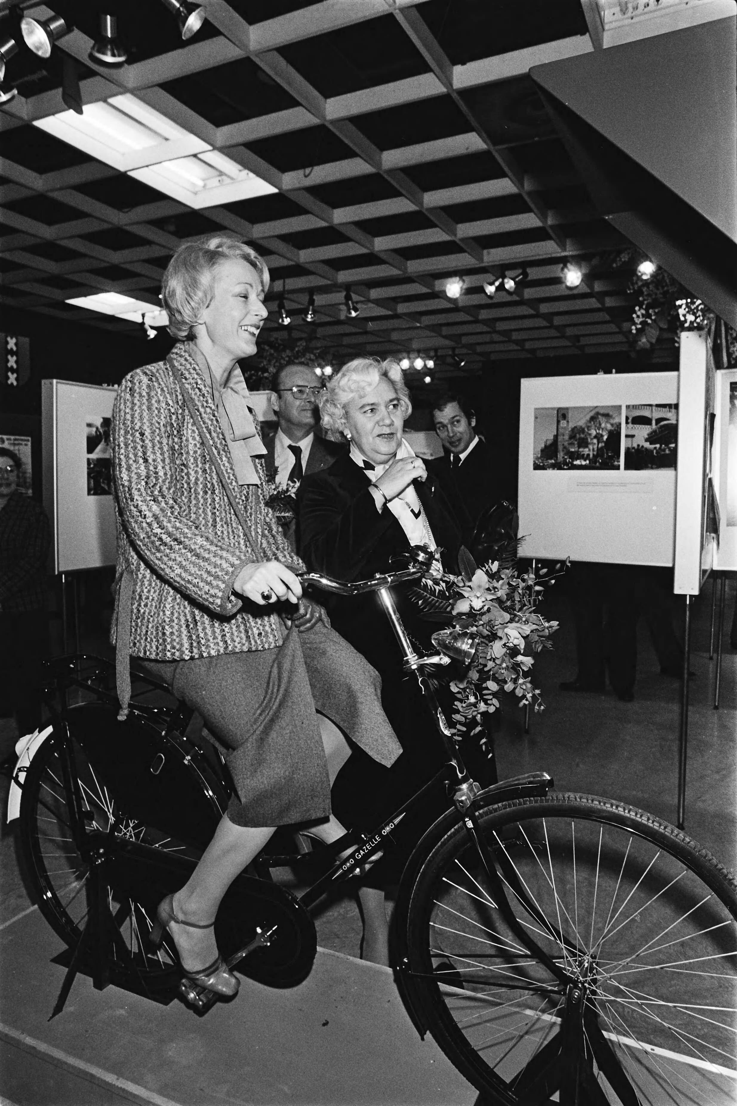 Fotocollectie Anefo — Mw Polak (burgemeester Polak) opent tent. over Amsterdam in V&D in Den Haag ; mw Schols (burgemeester schols) op fiets filmpje over Amsterdam — Foto: Dijk, Hans van / Anefo. Licentie: Set B: Rechtenvrij / Publiek Domein. Bron: Nationaal Archief. http://hdl.handle.net/10648/acda88ba-d0b4-102d-bcf8-003048976d84