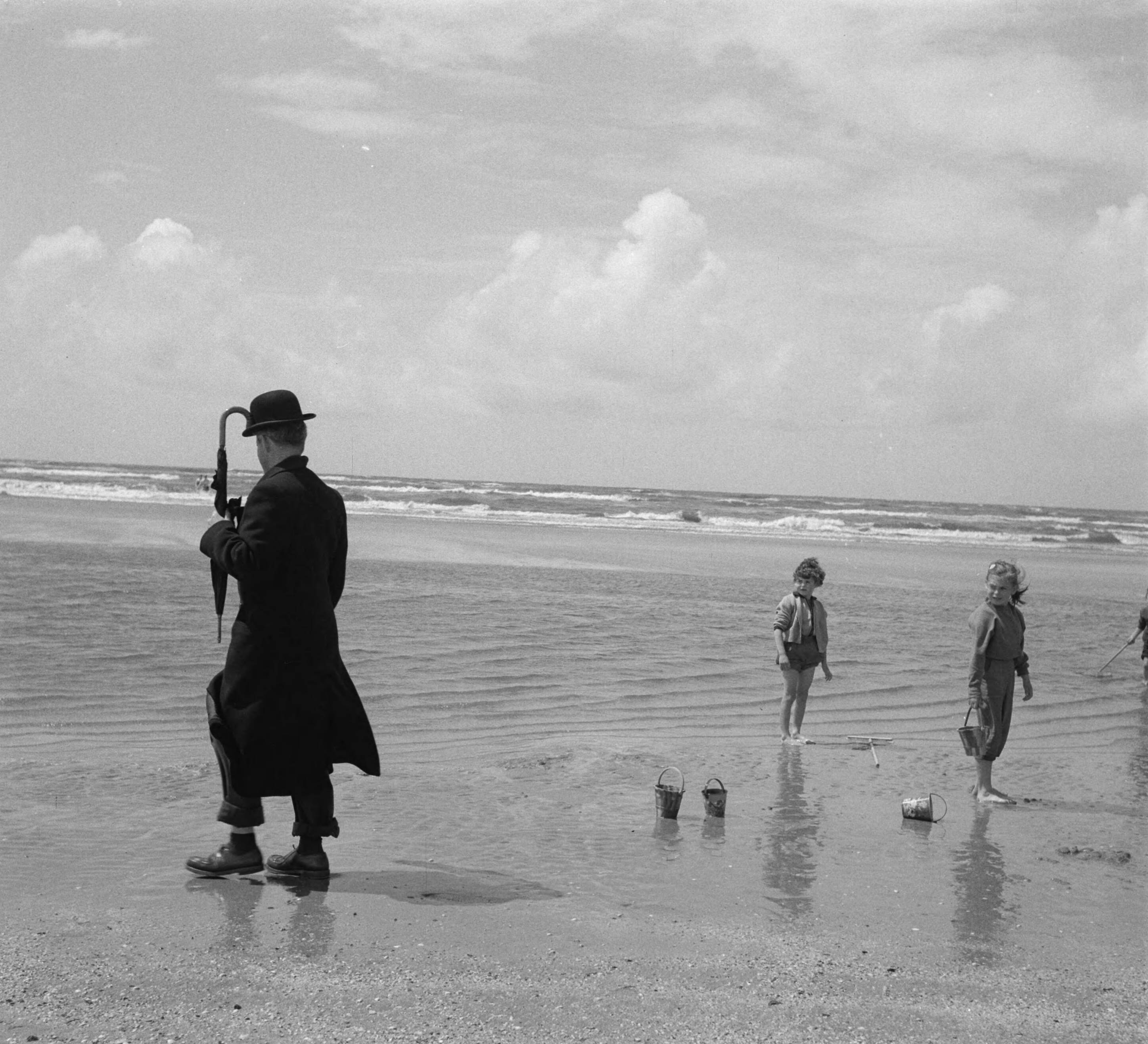 Fotocollectie Anefo — Zandvoort juni 1956. Een geklede oudere heer met paraplu en bolhoed kijkt naar spelende kinderen op het strand — Foto: Pot, Harry / Anefo. Licentie: Set B: Rechtenvrij / Publiek Domein. Bron: Nationaal Archief. http://hdl.handle.net/10648/a94a3858-d0b4-102d-bcf8-003048976d84