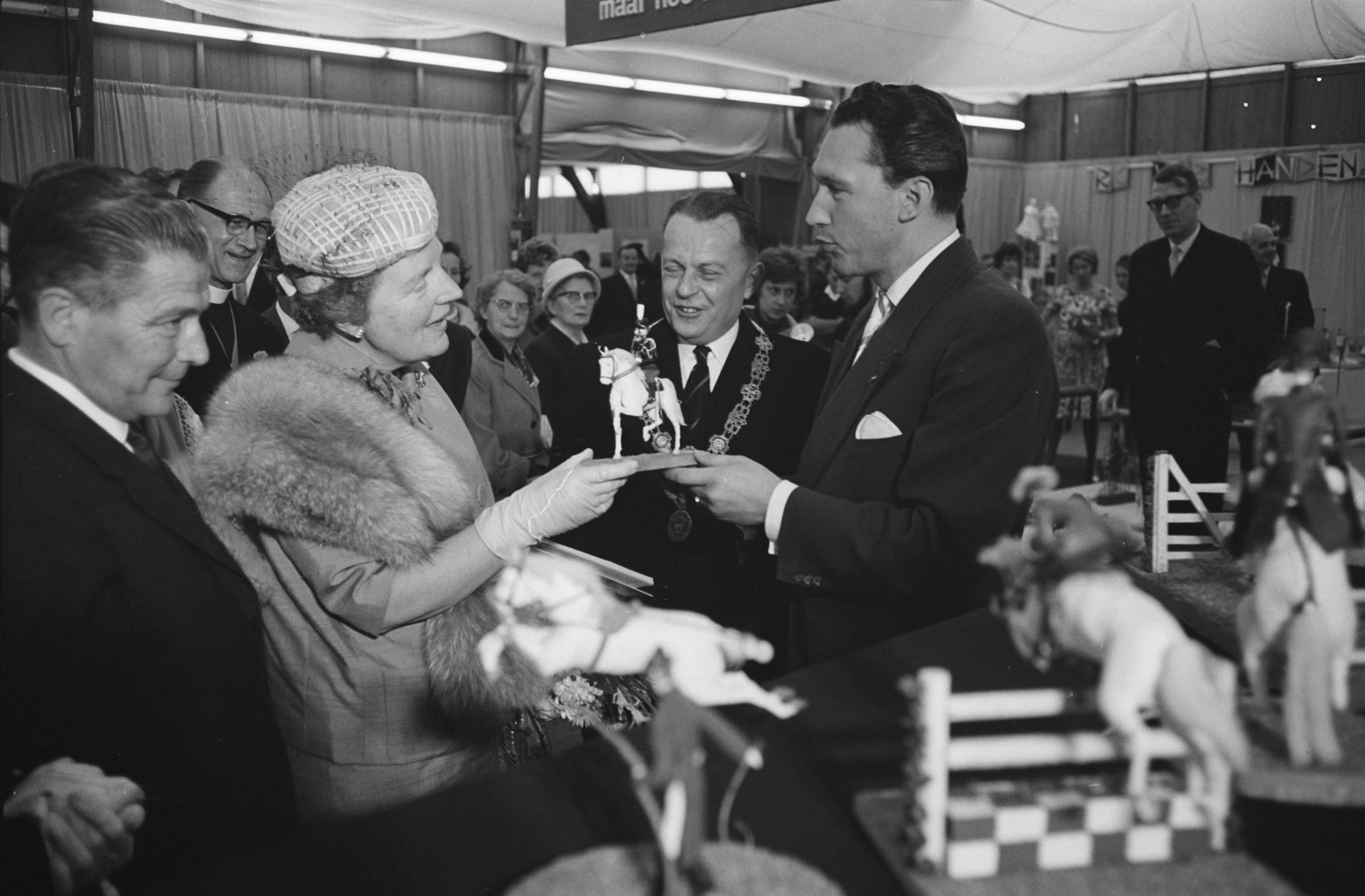 Fotocollectie Anefo — Koningin Juliana bezoekt tentoonstelling "Nu .... Breda 61 ". In de hobbyhal bood de heer H. van der Kroon haar een door hem zeil vervaardigd paardje met ruiter van leer aan, bestemd voor prinses Marijke — Foto: Pot, Harry / Anefo. Licentie: Set B: Rechtenvrij / Publiek Domein. Bron: Nationaal Archief. http://hdl.handle.net/10648/a9dd1952-d0b4-102d-bcf8-003048976d84