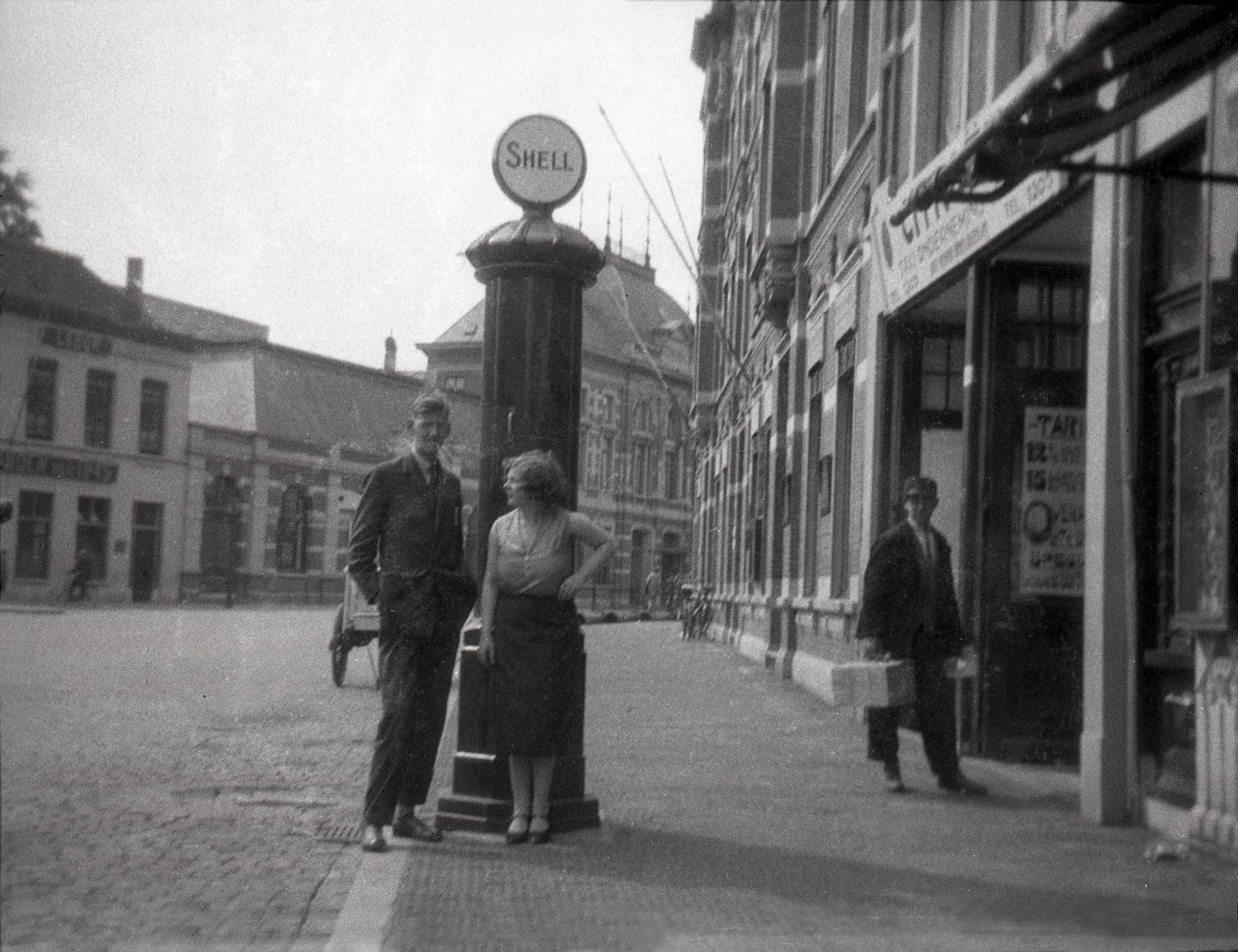Portretten, "Topografie, plaatsen op naam" — Portret van een onbekende man en een vrouw voor een Shell-benzinepomp [voor een taxi-onderneming] op het met kinderhoofdjes geplaveide Van Coothplein te Breda. Omstreeks 1928. De foto is afkomstig uit de collectie van portretfotograaf bekend onder de naam 'Atelier Anton Henning'. — Foto: Fotograaf onbekend / Fotobureau onbekend / Rechtenvrij (05889). Licentie: Set B: Rechtenvrij / Publiek Domein. Bron: Nationaal Archief. http://hdl.handle.net/10648/35429da6-64bf-a382-e063-6df0900a6686