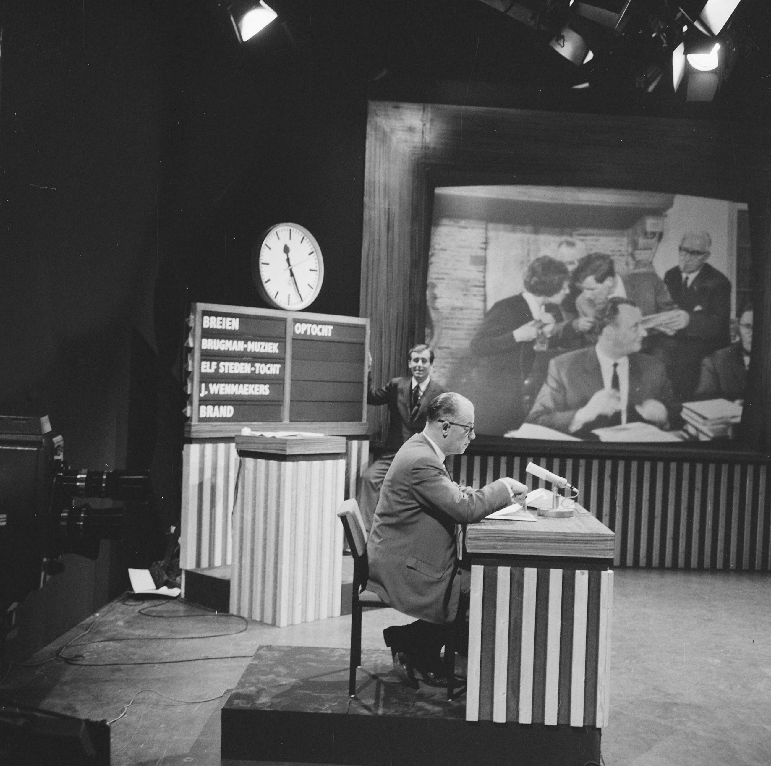 Fotocollectie Anefo — NCRV-quiz 'Een tegen allen' tussen Zierikzee en Bolsward, In de studio te Bussum, achter de desk de opdrachtengever, de heer Doeleman uit Zierikzee, daarachter spelleider Dick van Ruler, op het televisiescherm presentatrice Tanja Koen en burgemeester van Bolsward, J.A. Geukers in het stadhuis van Bolsward — Foto: Nijs, Jac. de / Anefo. Licentie: Set B: Rechtenvrij / Publiek Domein. Bron: Nationaal Archief. http://hdl.handle.net/10648/aa7f382c-d0b4-102d-bcf8-003048976d84