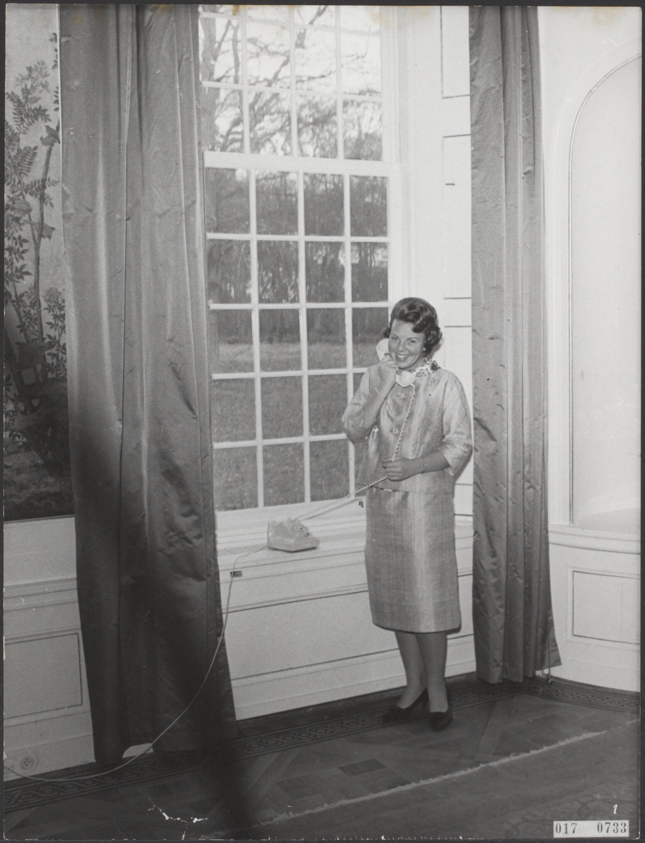 Fotocollectie Elsevier Binnenland — Serie: kasteel Drakensteyn bewoond door prinses Beatrix. Prinses Beatrix telefoneert staande voor een groot raam — Foto: ANP / RVD of rechtenvrij. Licentie: Set B: Rechtenvrij / Publiek Domein. Bron: Nationaal Archief. http://hdl.handle.net/10648/adbed5a6-d0b4-102d-bcf8-003048976d84