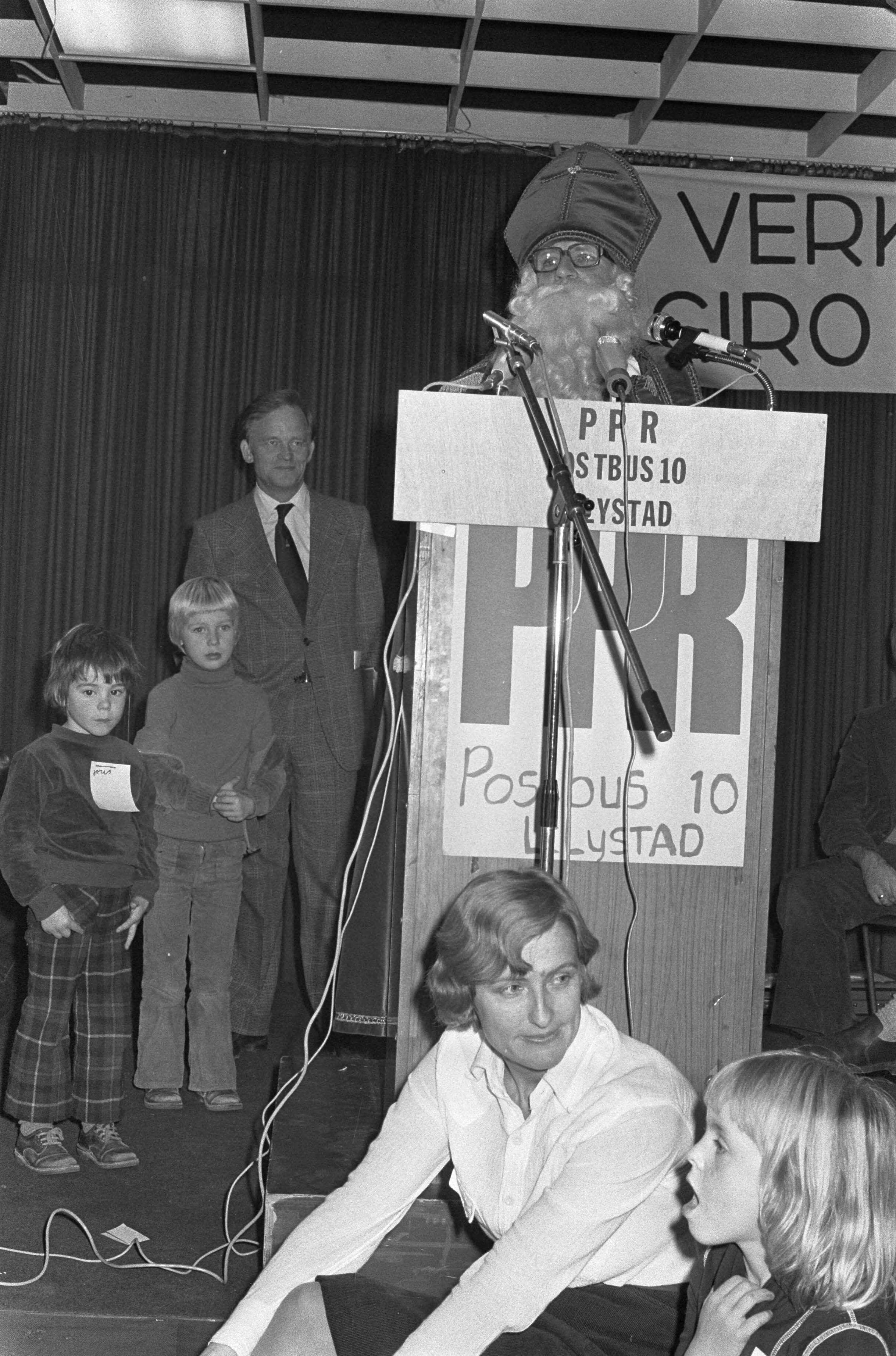 Fotocollectie Anefo — PPR-congres in Utrecht; minister Van Doorn als Sinterklaas aan het woord op voorgrond PPR-lijsttrekker Ria Beckers — Foto: Suyk, Koen / Anefo. Licentie: Set B: Rechtenvrij / Publiek Domein. Bron: Nationaal Archief. http://hdl.handle.net/10648/ac8fce2e-d0b4-102d-bcf8-003048976d84