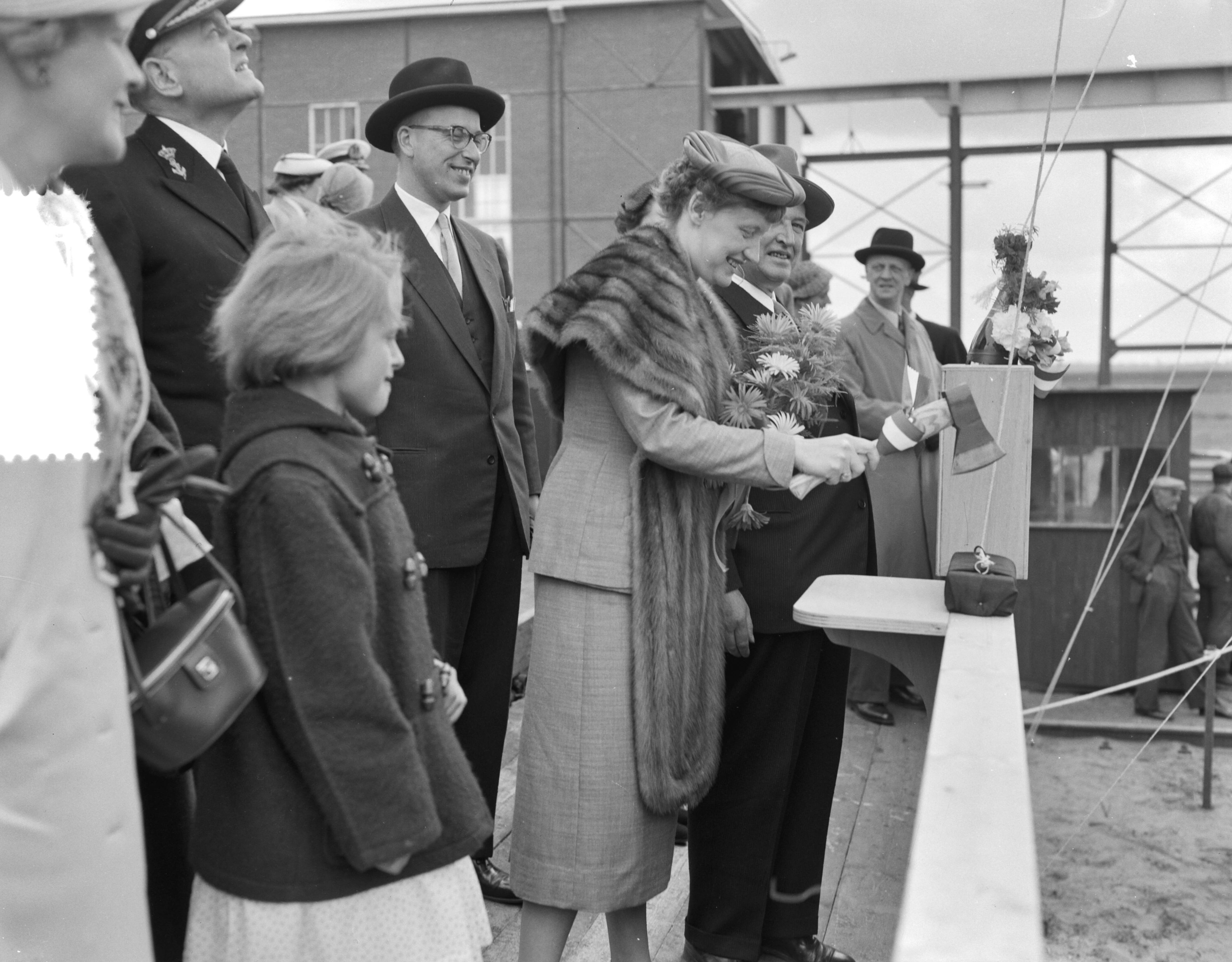 Fotocollectie Anefo — Tewaterlating van de mijnenveger Hr. Ms. "Lisse" bij scheepswerf E.J. Smit & Zn. te Westerbroek. De doopplechtigheid werd verricht door de echtgenote van de burgemeester van Lisse, mevr. W.H.M. de Graaf-Theuling. Haar man, Theo de Graaf met donkere hoed, achter haar — Foto: Rossem, Wim van / Anefo. Licentie: Set B: Rechtenvrij / Publiek Domein. Bron: Nationaal Archief. http://hdl.handle.net/10648/a9483328-d0b4-102d-bcf8-003048976d84