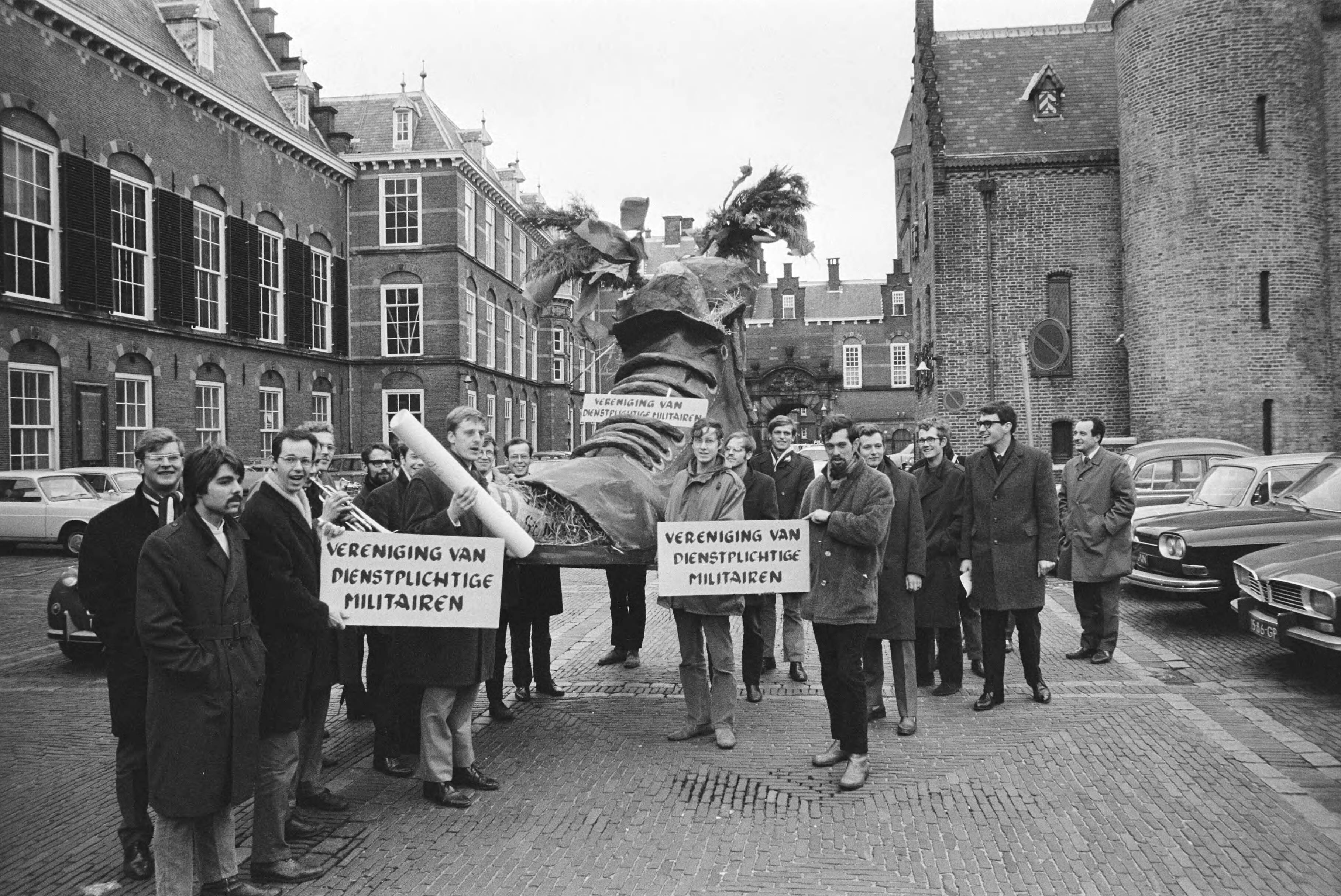 Fotocollectie Anefo — Vereniging van dienstplichtige militairen biedt schoen met verlanglijst aan aan leden Tweede Kamer , Binnenhof, Den Haag — Foto: Evers, Joost / Anefo. Licentie: Set B: Rechtenvrij / Publiek Domein. Bron: Nationaal Archief. http://hdl.handle.net/10648/abac1864-d0b4-102d-bcf8-003048976d84