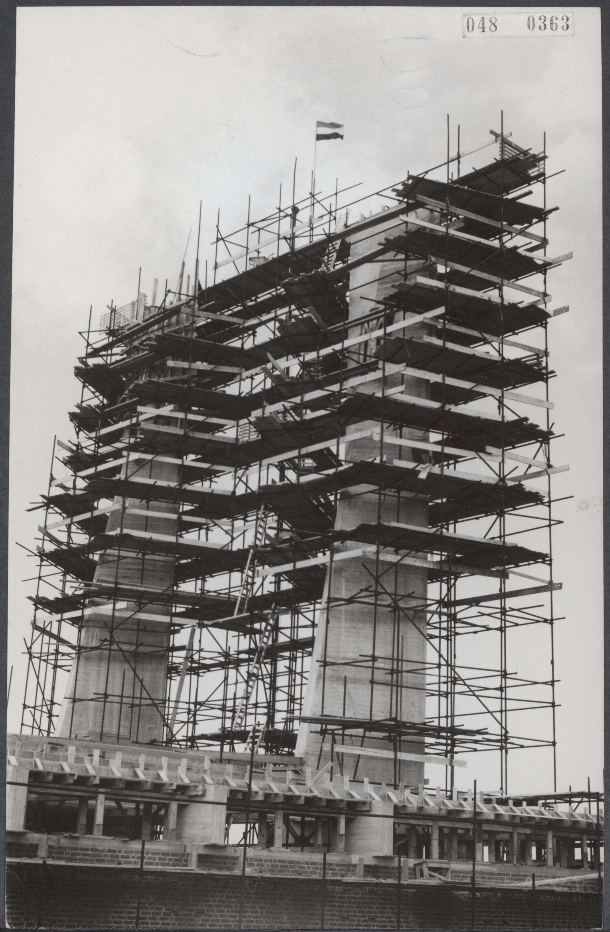 Fotocollectie Elsevier Binnenland — De linkertoren van de in aanbouw zijnde Fonteinkerk te Voorburg heeft zijn hoogste punt bereikt. Reeds eerder was de rechtertoren klaar gekomen. Beide hebben een hoogte van 30 meter en er is bij elk 100 m3 beton nodig geweest — Foto: Behrens, Herbert F. / Anefo. Licentie: Set B: Rechtenvrij / Publiek Domein. Bron: Nationaal Archief. http://hdl.handle.net/10648/ae012492-d0b4-102d-bcf8-003048976d84