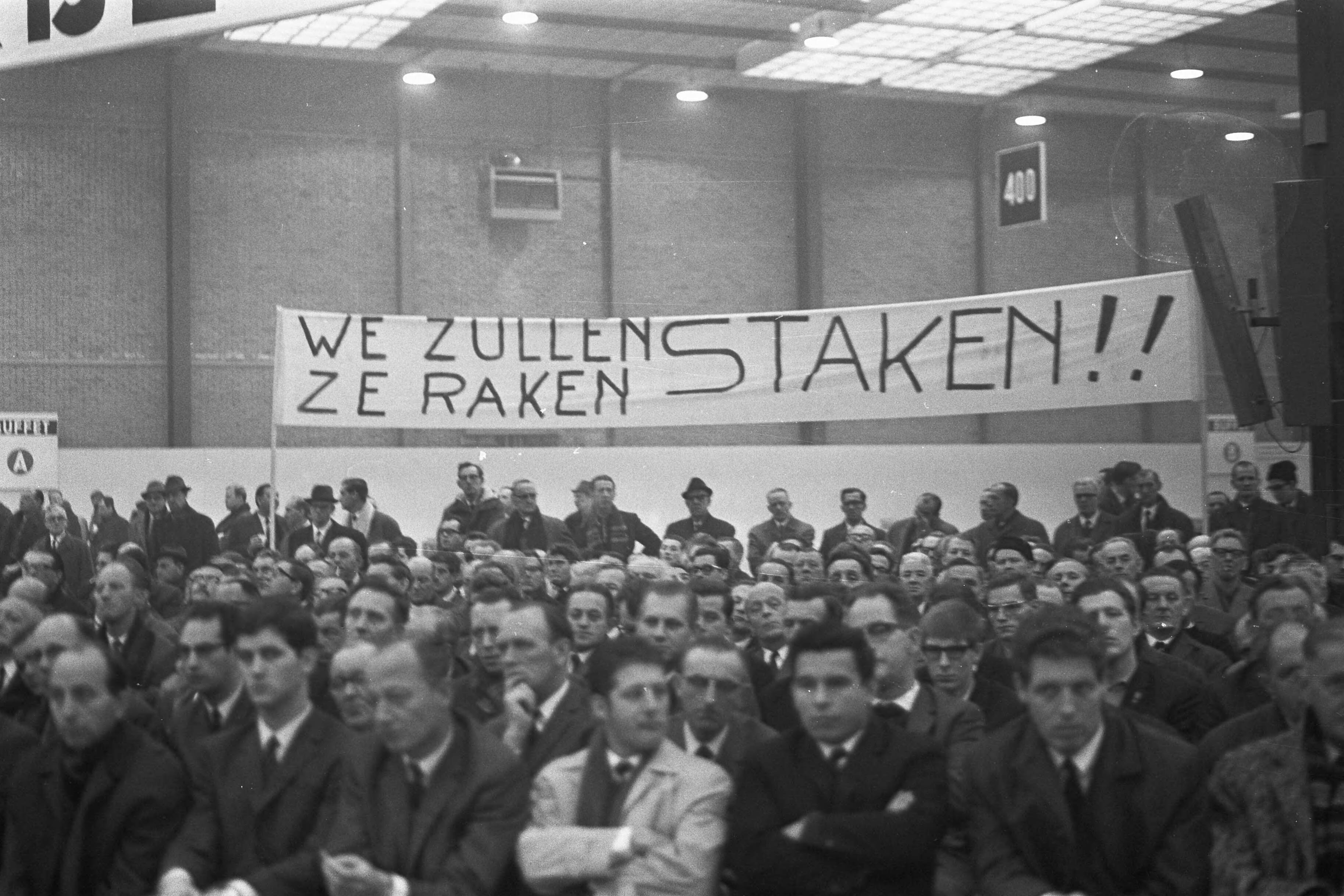Fotocollectie Anefo — Metaalarbeiders van het NVV bijeen in Utrecht i.v.m. nieuwe CAO 23 : spandoek "We zullen ze raken, staken!!", 24 , 25, 26: M. Zondervan (voorz. metaalbedrijfs / — Foto: Nijs, Jac. de / Anefo. Licentie: Set B: Rechtenvrij / Publiek Domein. Bron: Nationaal Archief. http://hdl.handle.net/10648/ab573146-d0b4-102d-bcf8-003048976d84