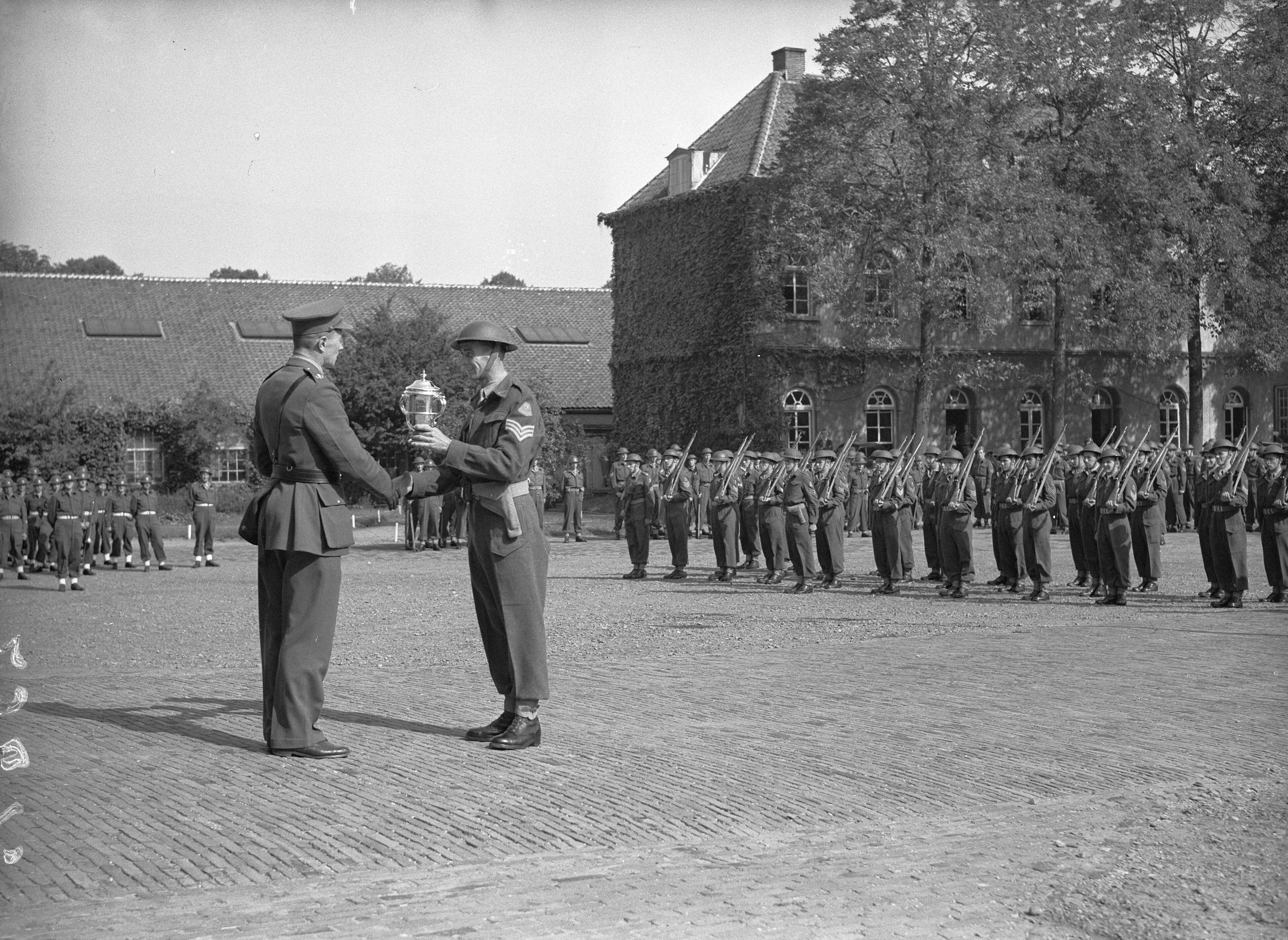 Fotocollectie Anefo — Afscheidsparade opleidingscursus Reserve-officieren Breda. Uitreiking beker voor sportwedstrijden door een kolonel aan een sergeant op de paradeplaats van de KMA — Foto: Wisman, Bram / Anefo. Licentie: Set B: Rechtenvrij / Publiek Domein. Bron: Nationaal Archief. http://hdl.handle.net/10648/a8ad0150-d0b4-102d-bcf8-003048976d84