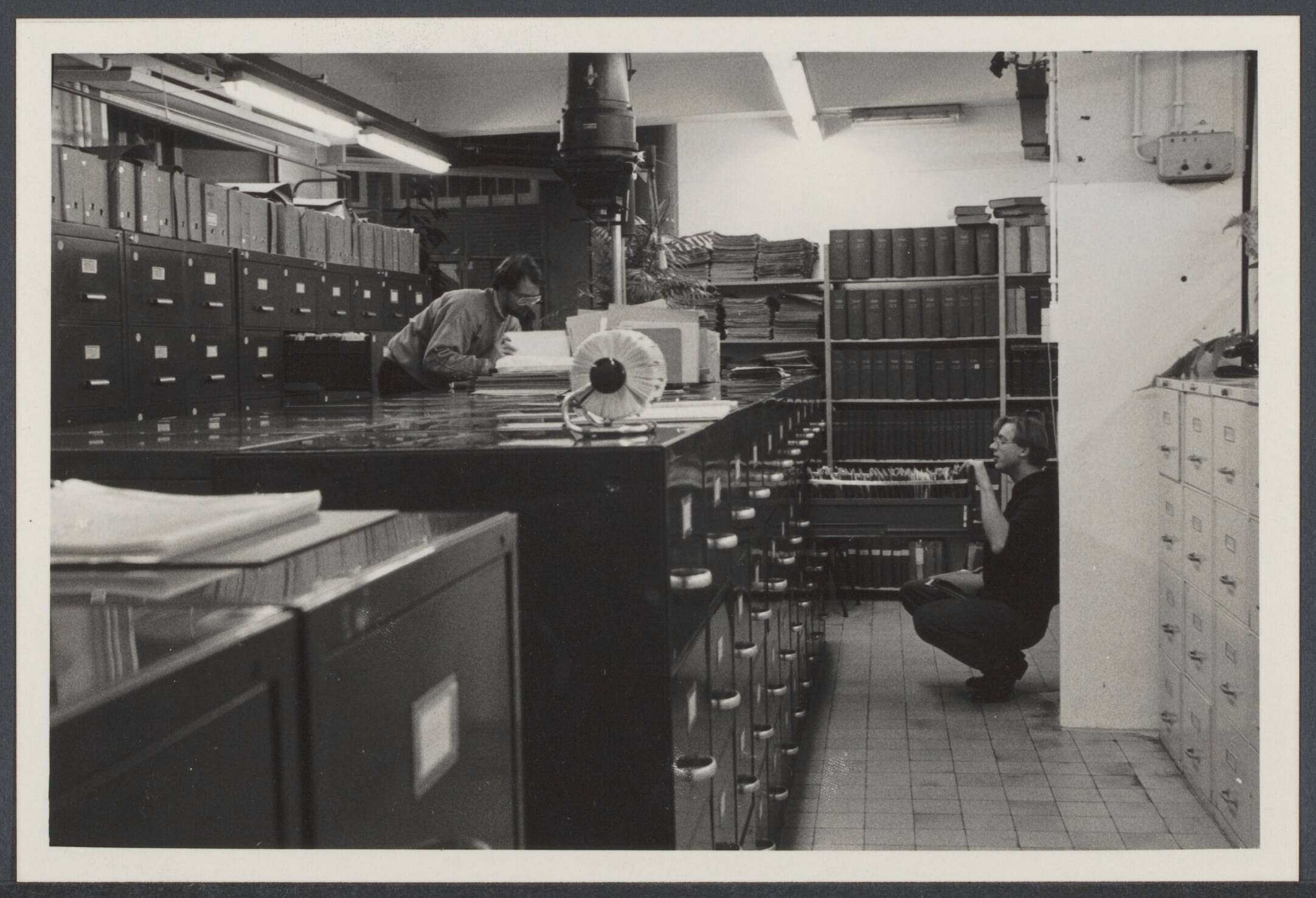 Fototheek, fotothecaris : Spaarnestad Fotoarchief. — Spaarnestad fotoarchief in oude zegeldrukkerij Joh. Enschedé, Haarlem ca. 1990. Links Freek Baars, rechts Frido Troost — Foto: Fotograaf Onbekend / Spaarnestad. Licentie: Set B: Rechtenvrij / Publiek Domein. Bron: Nationaal Archief. http://hdl.handle.net/10648/1bee522a-3309-6742-09c4-a63043c15999