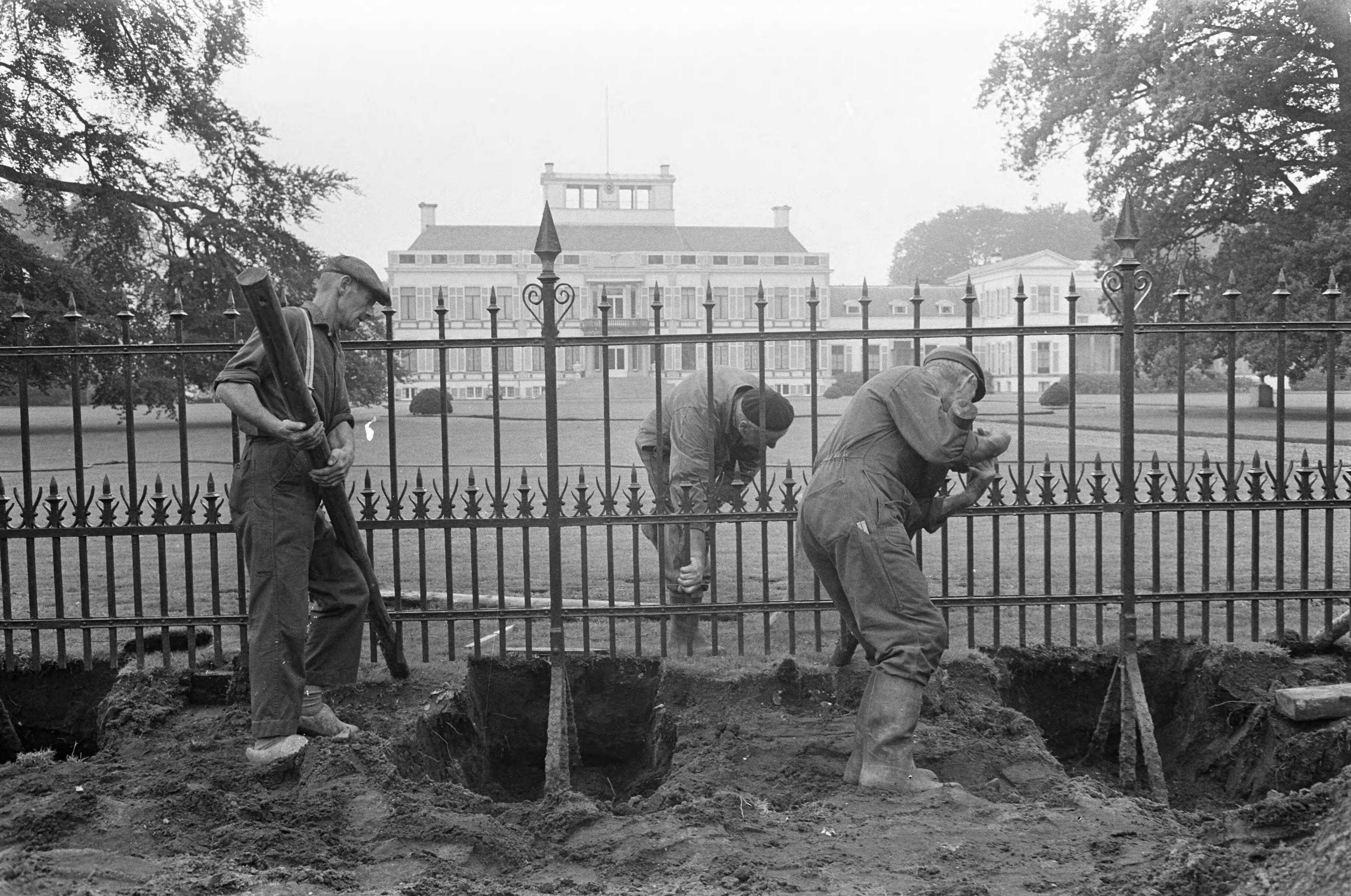 Aanleg van een vierbaansweg voor Paleis Soestdijk — Het opnieuw rechtzetten van het hek rond de paleistuin — Foto: Fotograaf Onbekend / Anefo. Licentie: Set B: Rechtenvrij / Publiek Domein. Bron: Nationaal Archief. http://hdl.handle.net/10648/ab496818-d0b4-102d-bcf8-003048976d84