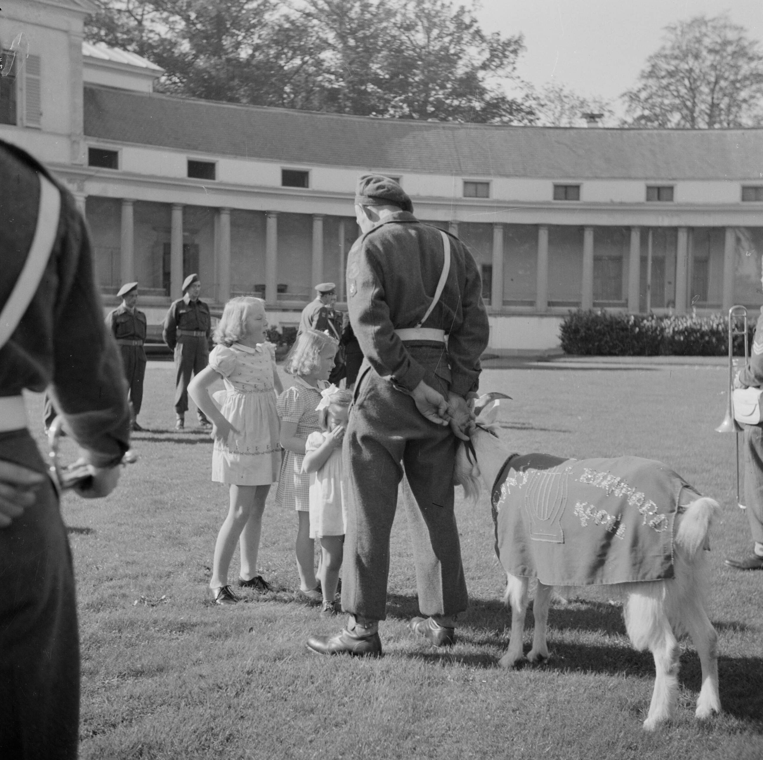 Afscheid in de voortuin van paleis Soestdijk van de Prins Bernhard Kapel met hun mascotte, de geit Kees, wegens vertrek naar Nederlands-Indië — muziekkorpsen|geiten|prinsen|prinsessen|paleizen|Paleis Soestdijk|Beatrix (prinses Nederland)|Margriet (prinses Nederland)|Bernhard (prins Nederland)|Irene (prinses Nederland)|Baarn|Utrecht (provincie)|koninklijk huis — Foto: Poll, Willem van de. Licentie: Set B: Rechtenvrij / Publiek Domein. Bron: Nationaal Archief. http://hdl.handle.net/10648/aee88a94-d0b4-102d-bcf8-003048976d84