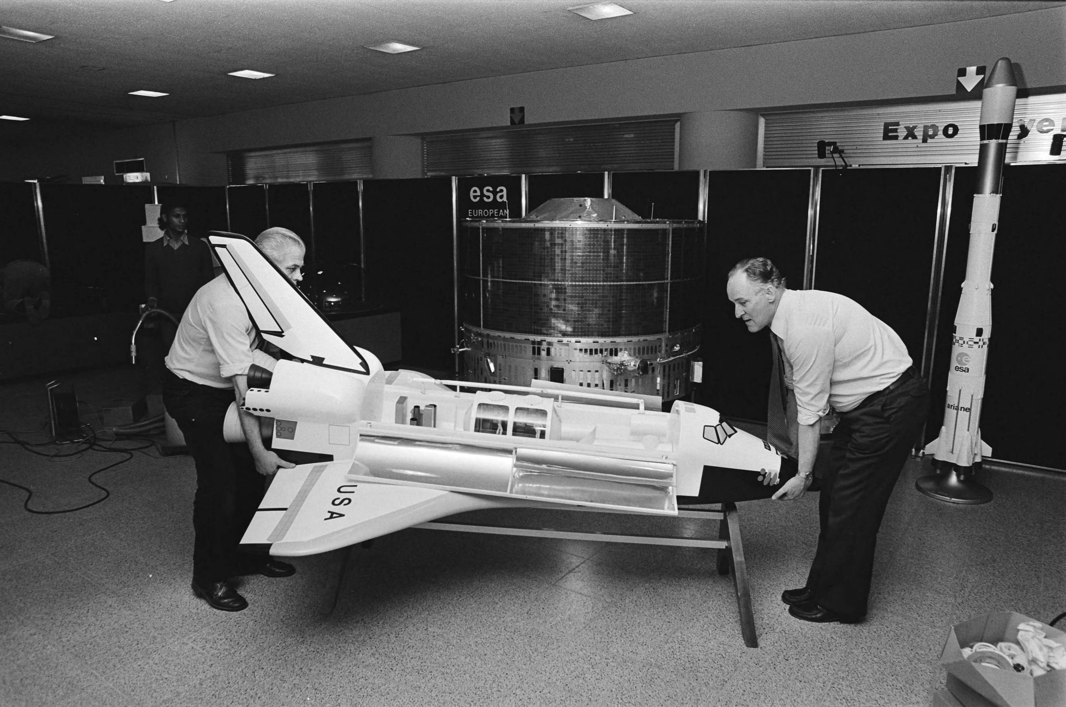 Fotocollectie Anefo — Morgen Sterrekunde-dag in Congrescentrum in Den Haag georganiseerd door Teleac, 2 medewerkers van ESA plaatsen model van Amerikaanse Space-shuttle — Foto: Antonisse, Marcel / Anefo. Licentie: Set B: Rechtenvrij / Publiek Domein. Bron: Nationaal Archief. http://hdl.handle.net/10648/acf6f0b8-d0b4-102d-bcf8-003048976d84
